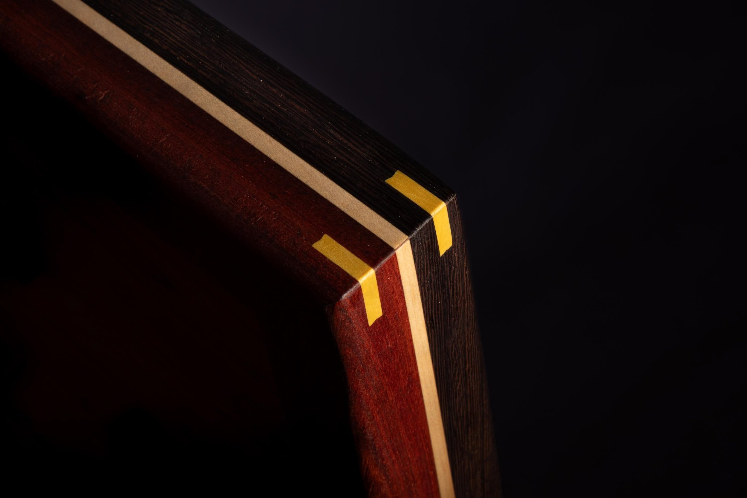 Close-up of the edge of a wooden object with yellow markings, showing layered wood in dark and reddish hues.