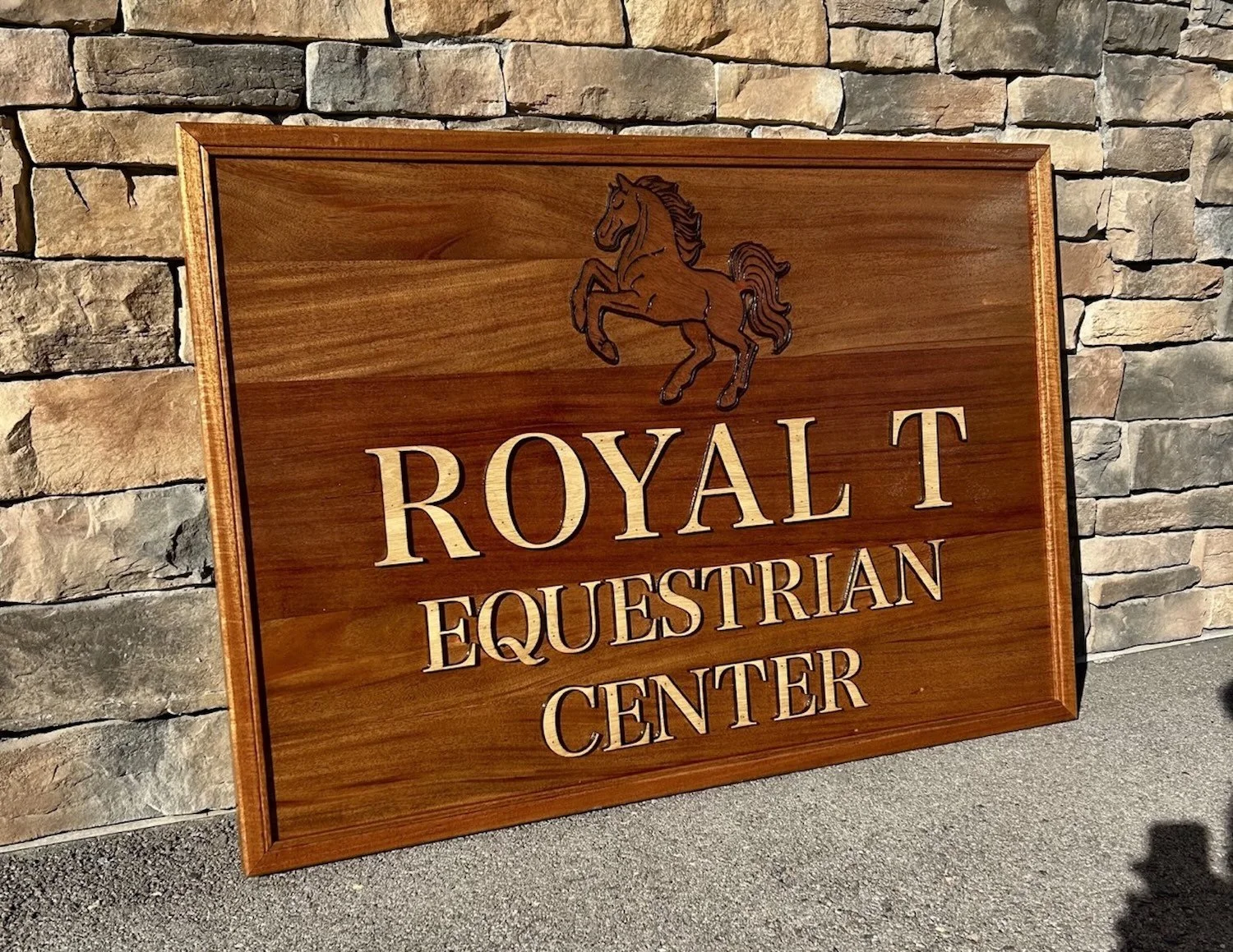 Wooden sign for Royal Equestrian Center with a horse illustration, placed against a stone wall.