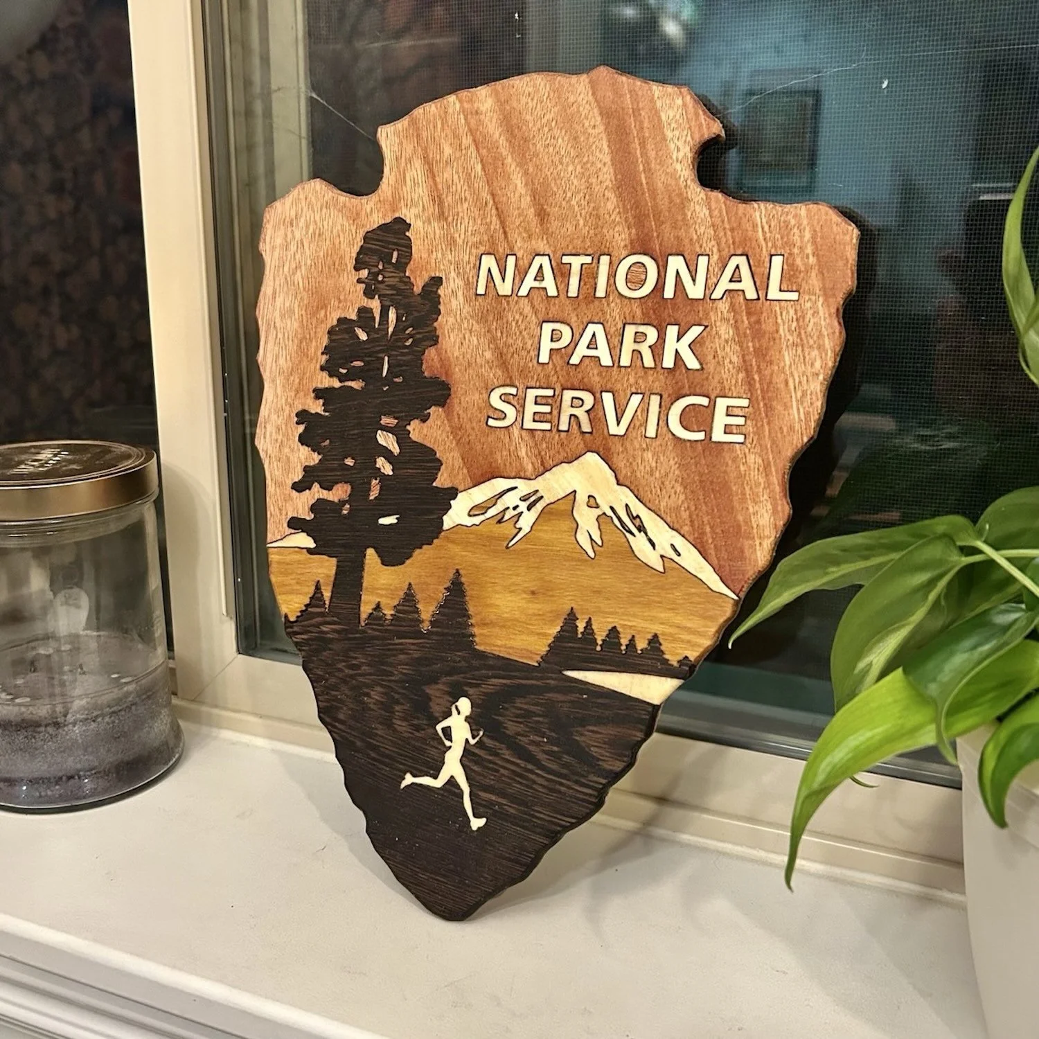 Wooden sign with the text 'National Park Service' and a graphic of a pine tree, mountain, and a person running.
