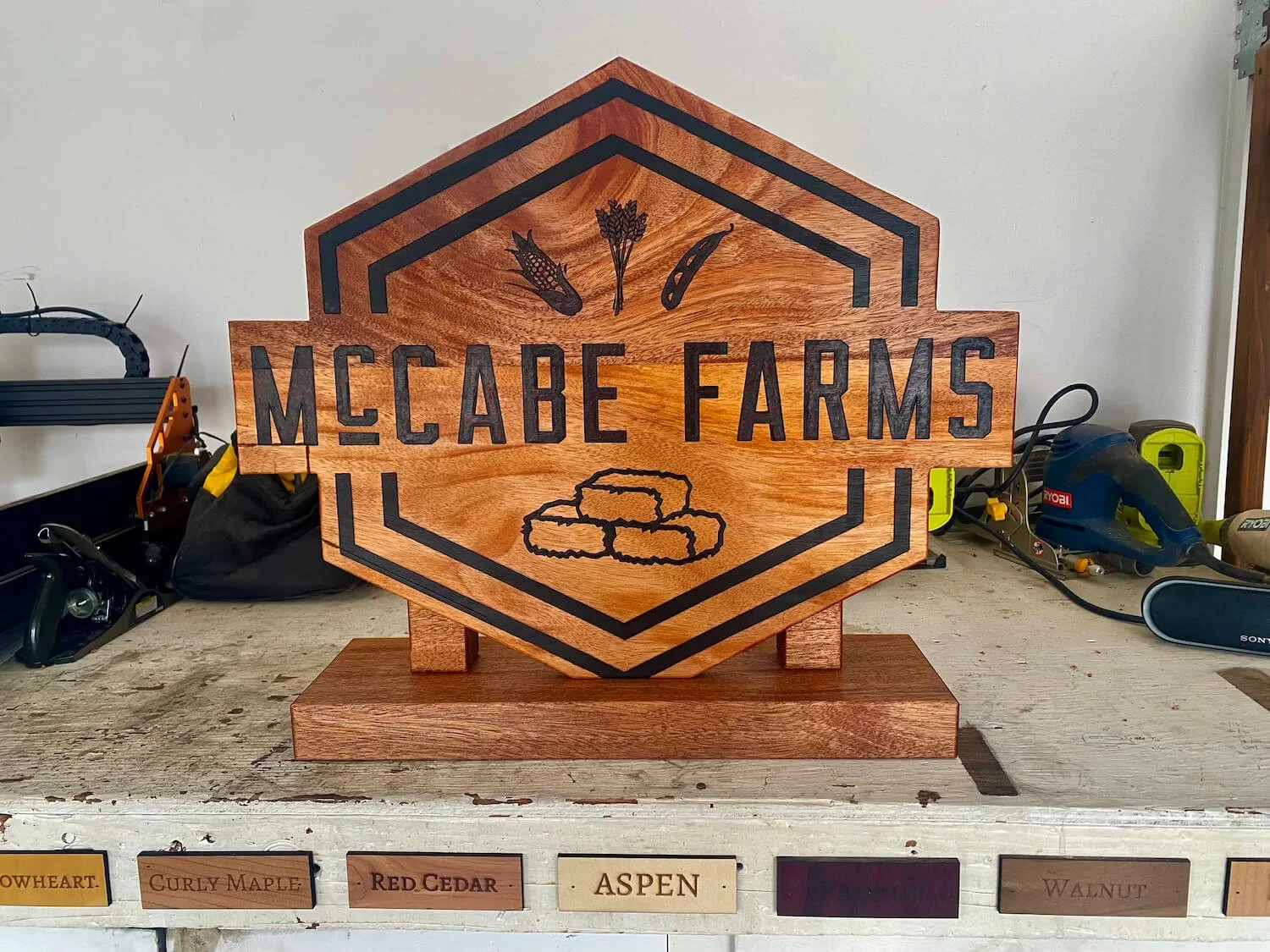 Wooden sign for McCabe Farms with black lettering and images of corn, wheat, and barley on a workbench surrounded by tools.