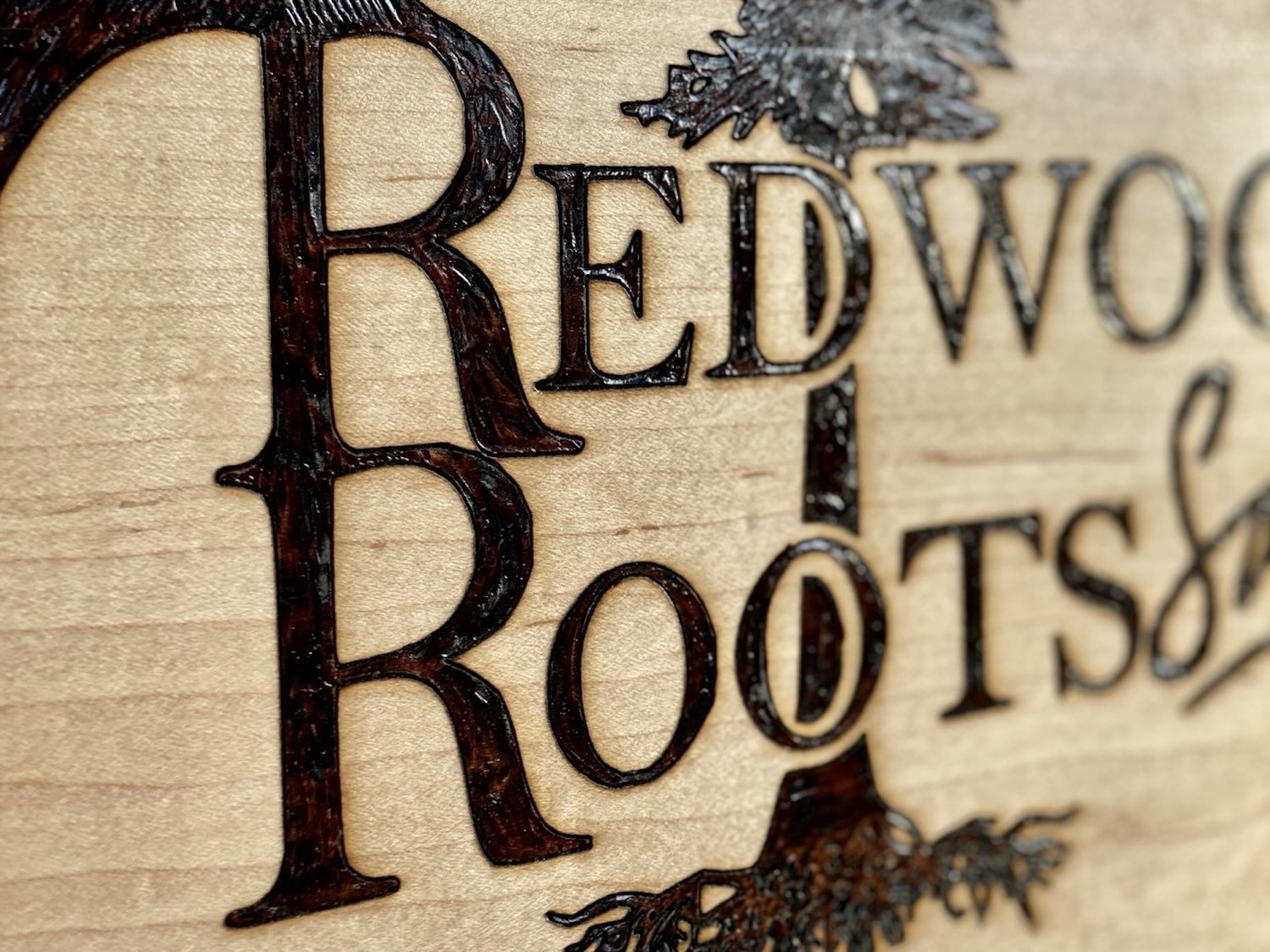 Close-up of a wooden plaque with engraved text and decorative elements, reading 'Redwood Roots Salon'.