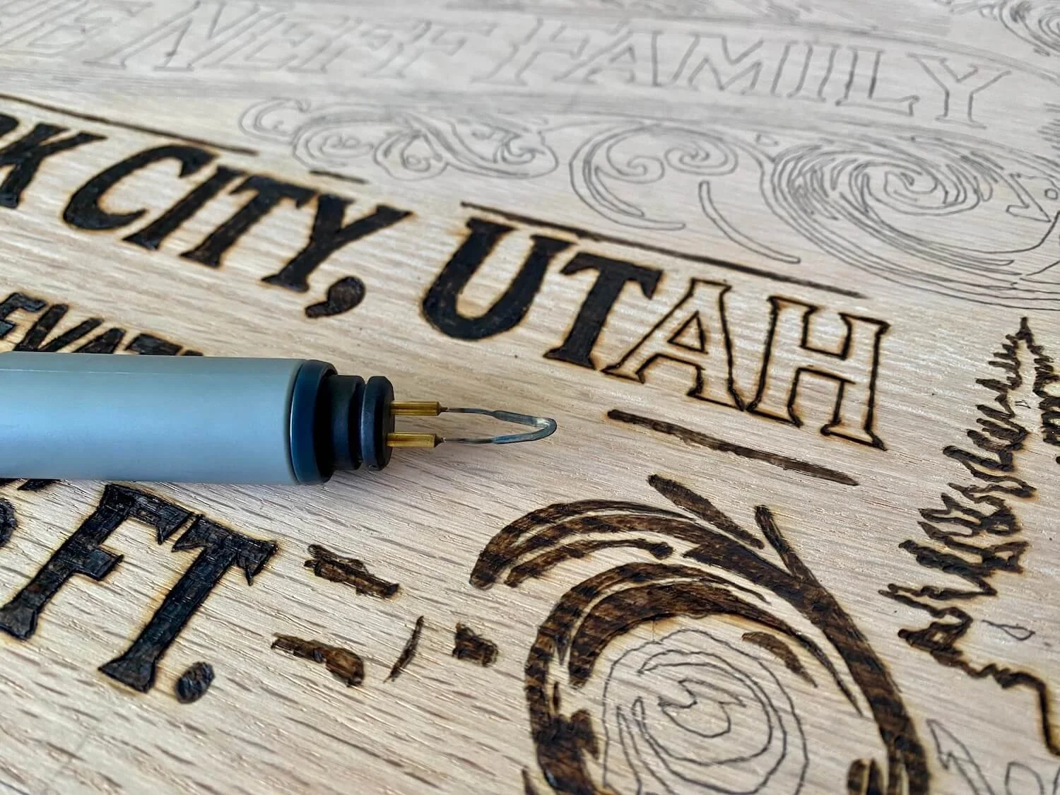 A close up shot of a wired-tip pyrography tool laying on top of a half completed wood burning piece.