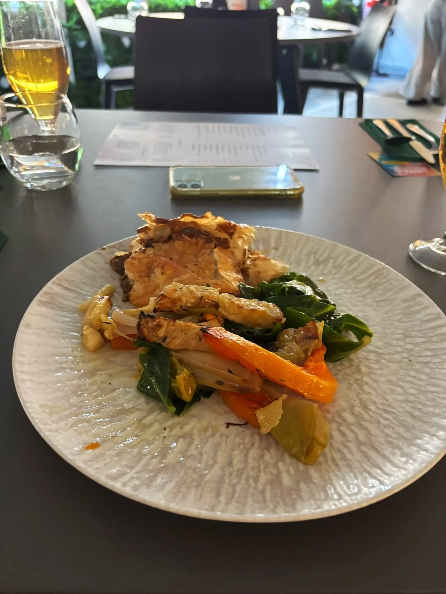 A white plate with grilled chicken, sautéed green vegetables, and roasted carrots on a table.