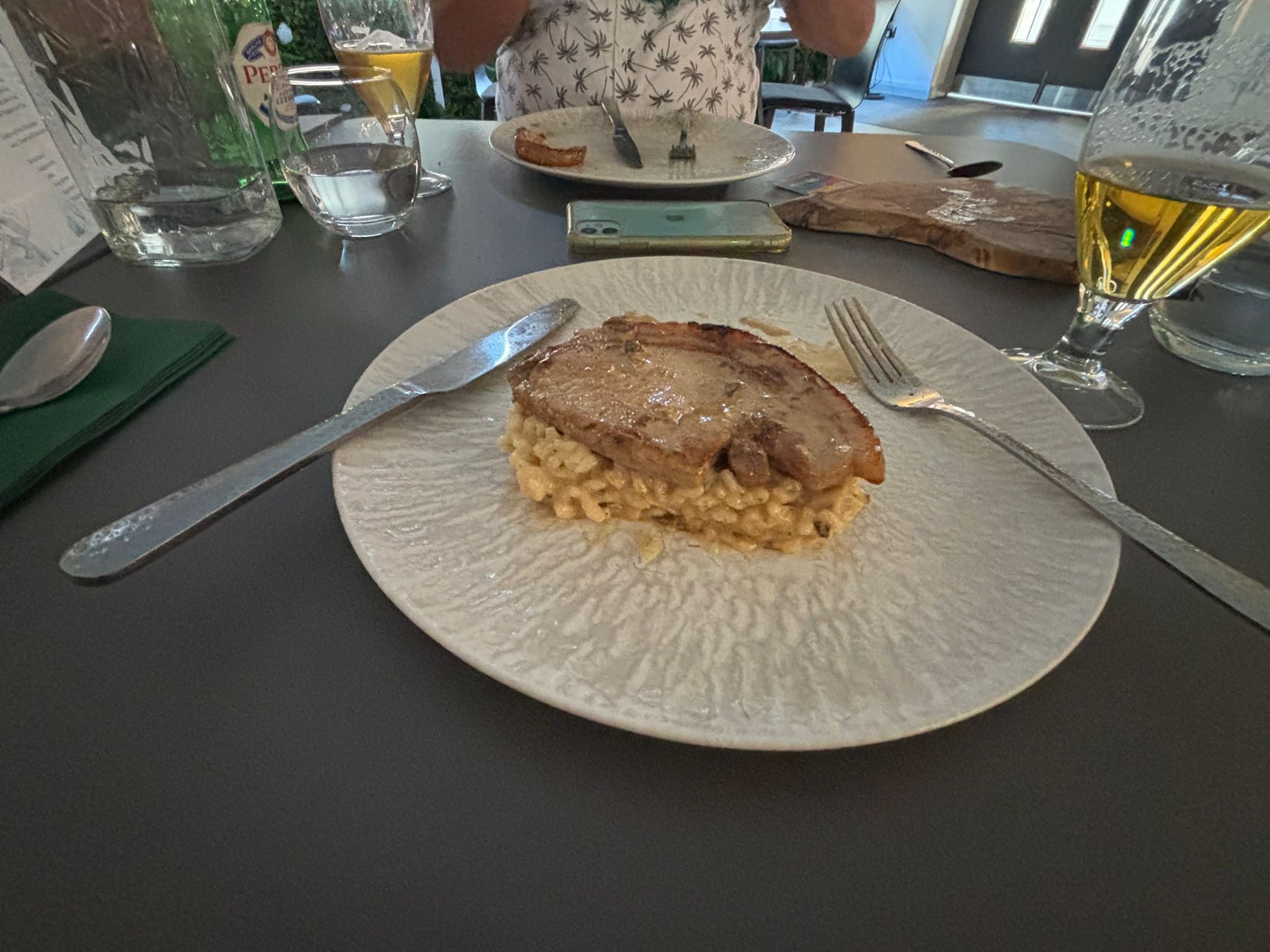 A close-up view of a plate with a serving of chicken and mashed potatoes on a dining table, with drinks and utensils visible in the background.