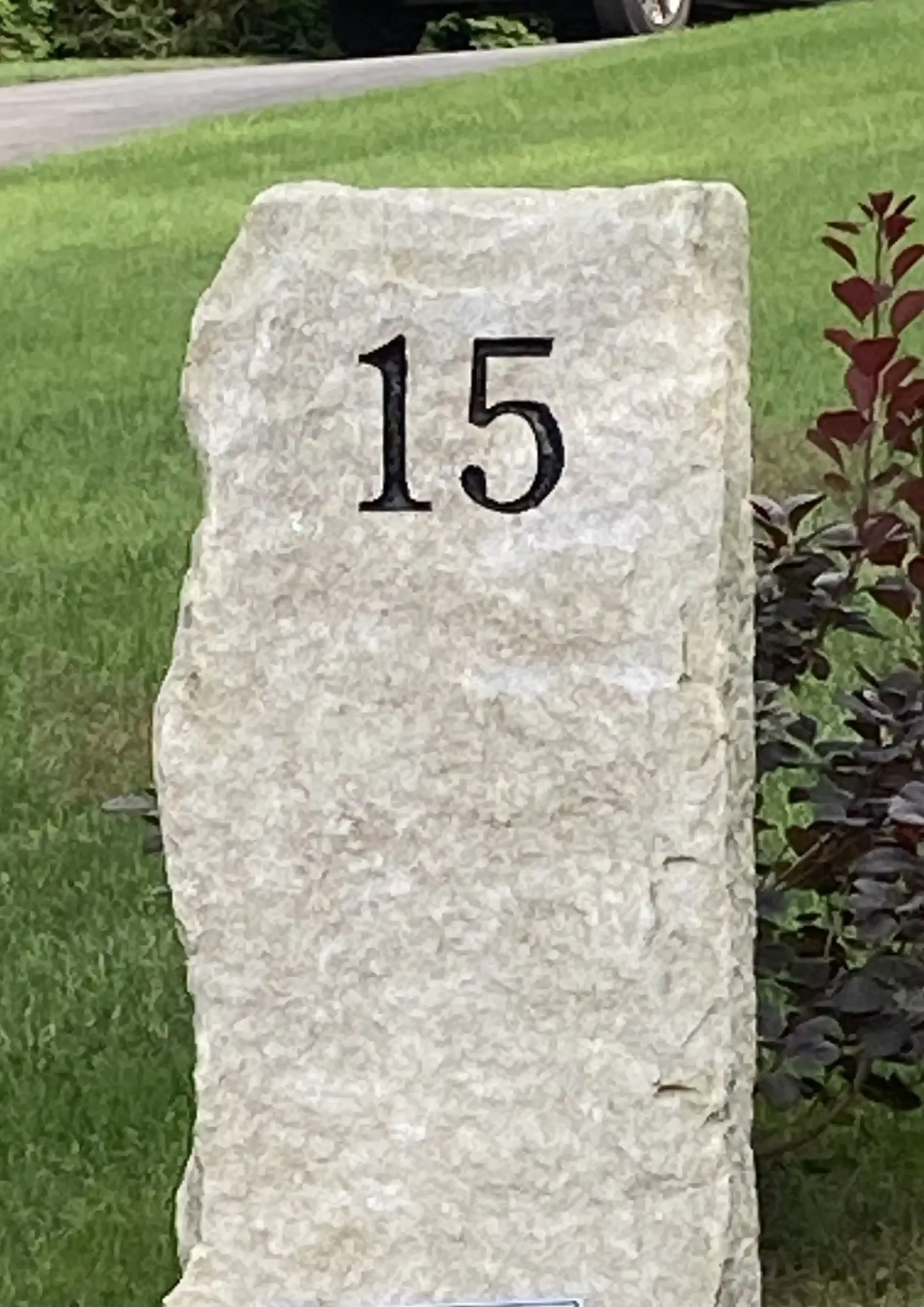 An address stone with the number 15 engraved on it, located next to a grass lawn.