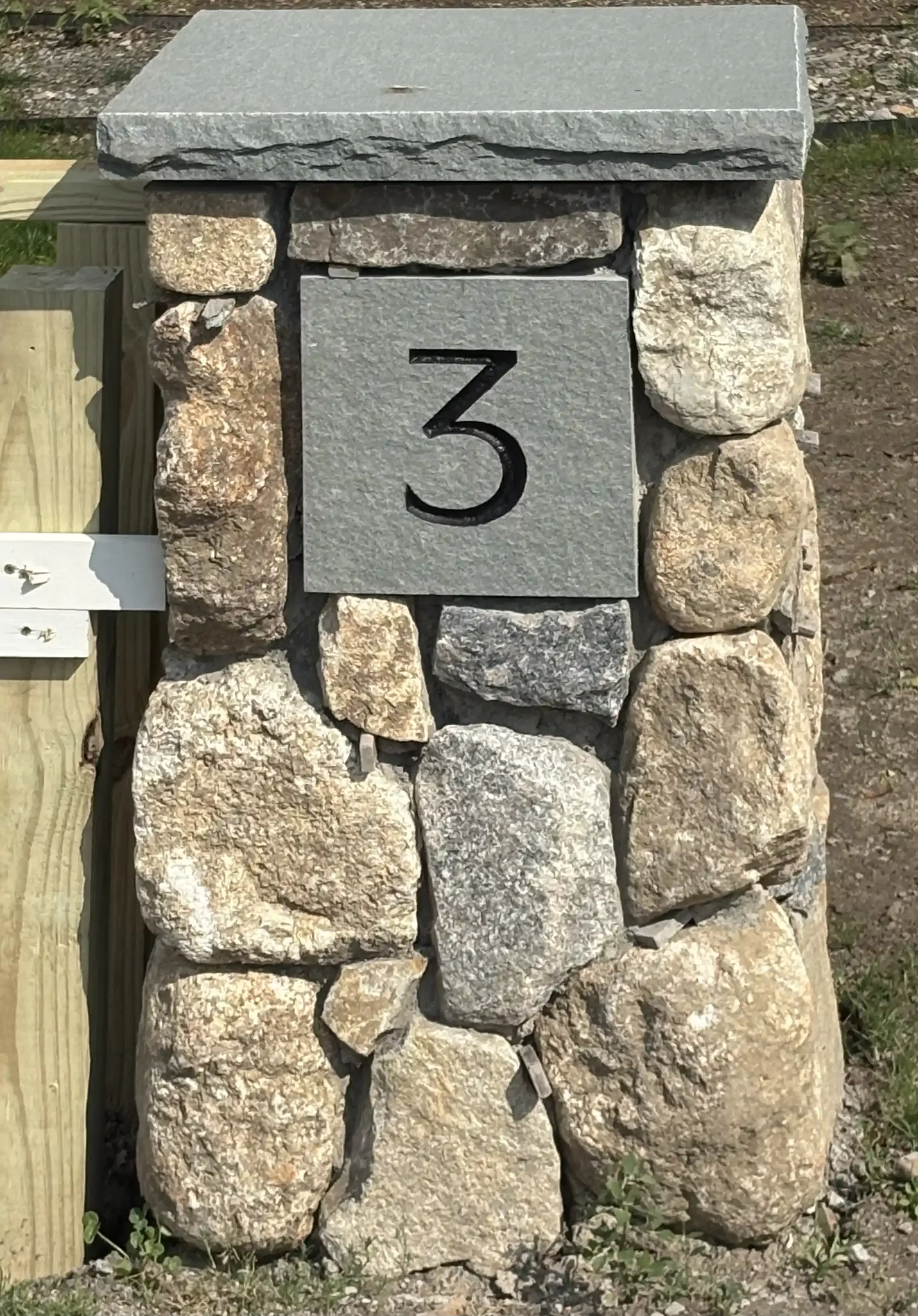 A stone column with the number 3 engraved on a rectangular gray stone plaque, surrounded by large rocks and situated outdoors.