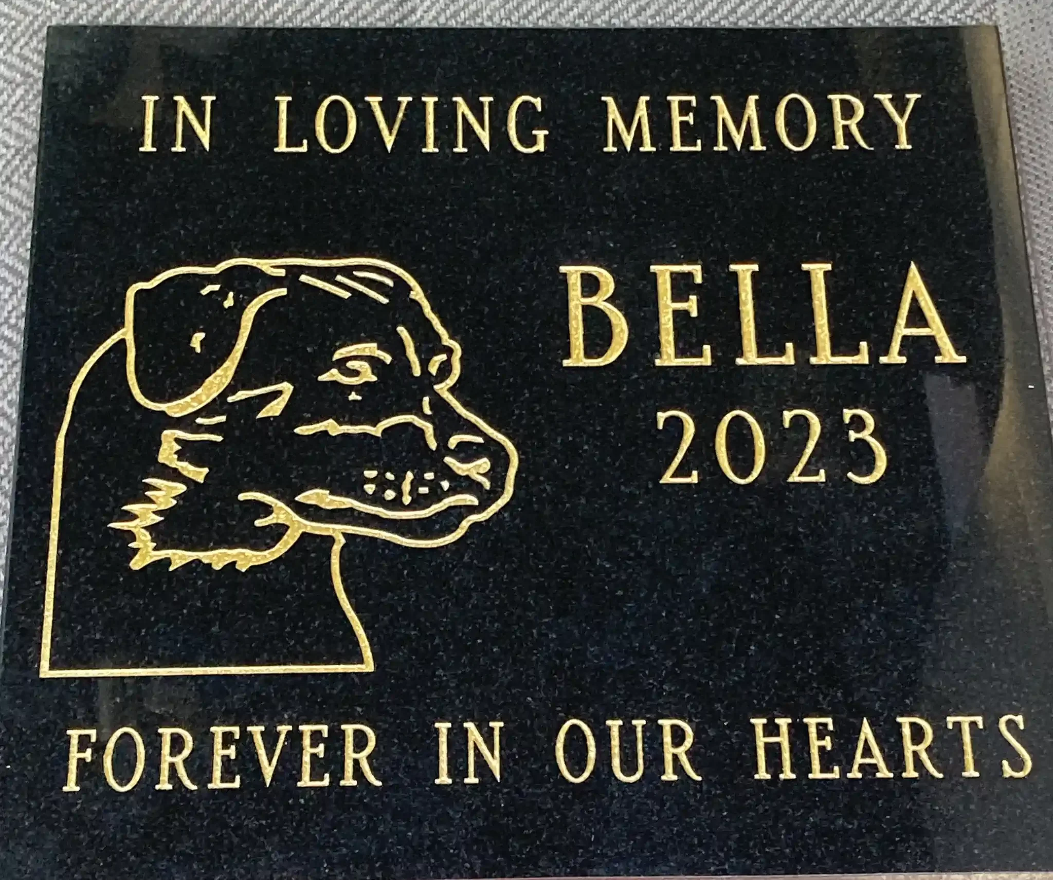 A black memorial plaque with gold text and a gold outline of a dog's head.
