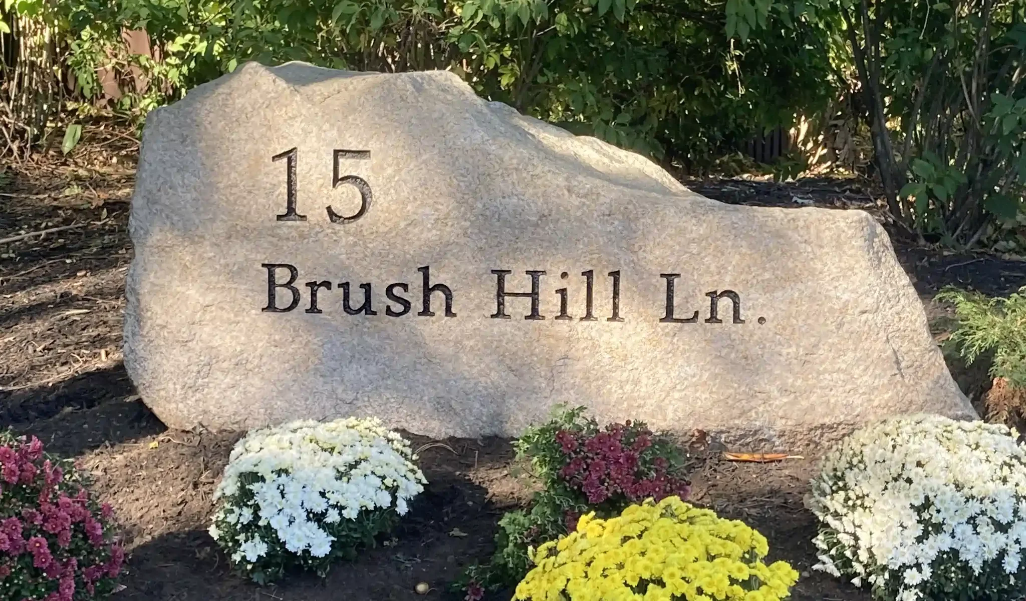 A large address stone with the number 15 engraved on it, surrounded by colorful flowers and greenery.