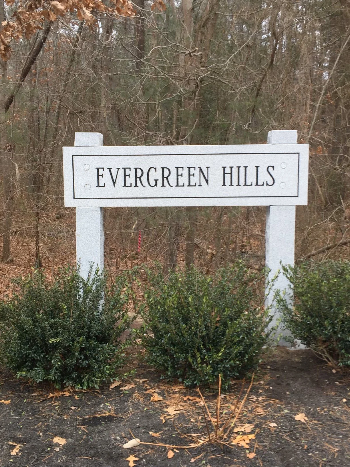 A granite sign for Evergreen Hills in front of trees and bushes.