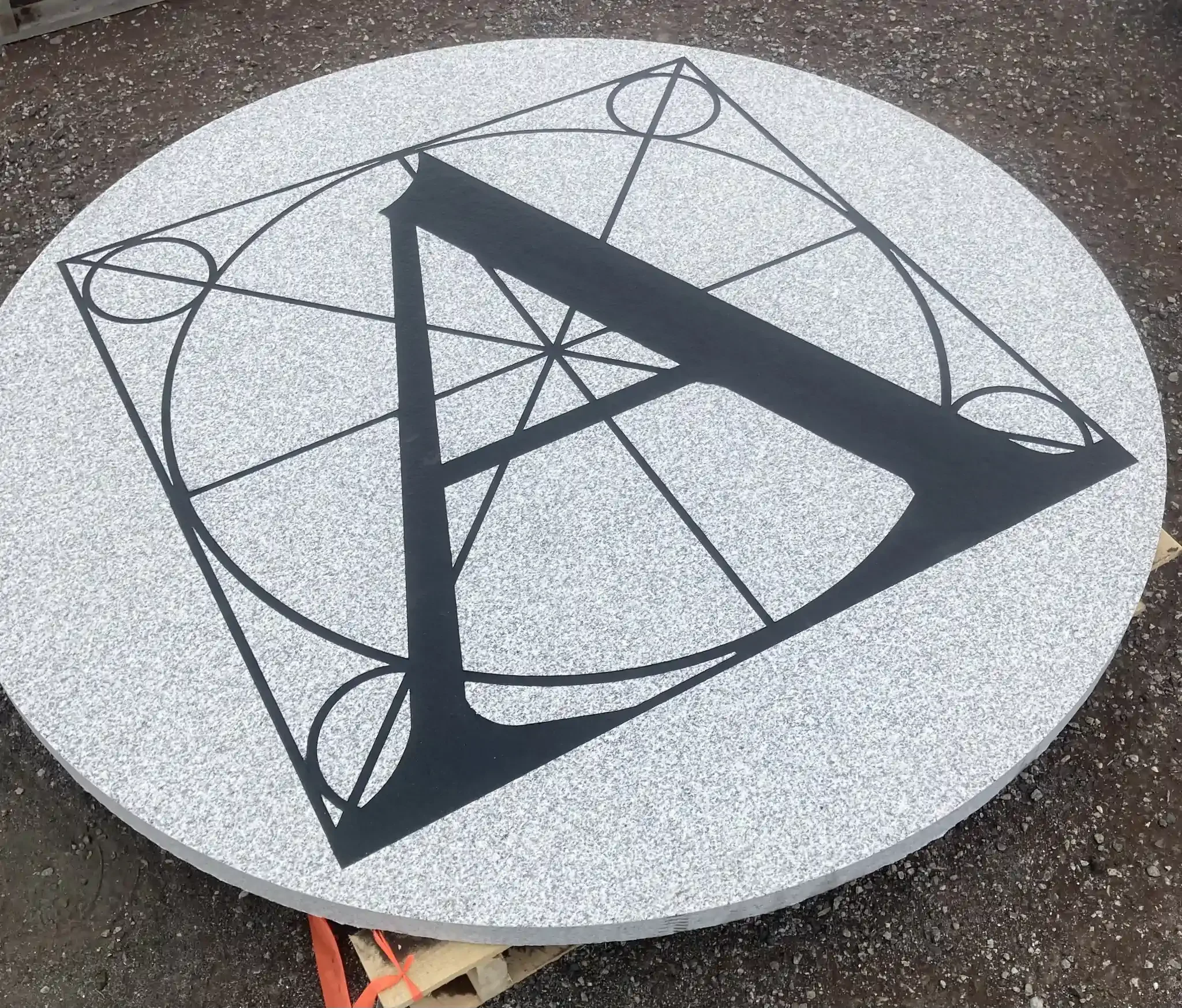 Round granite piece featuring a black line drawing with the letter A.