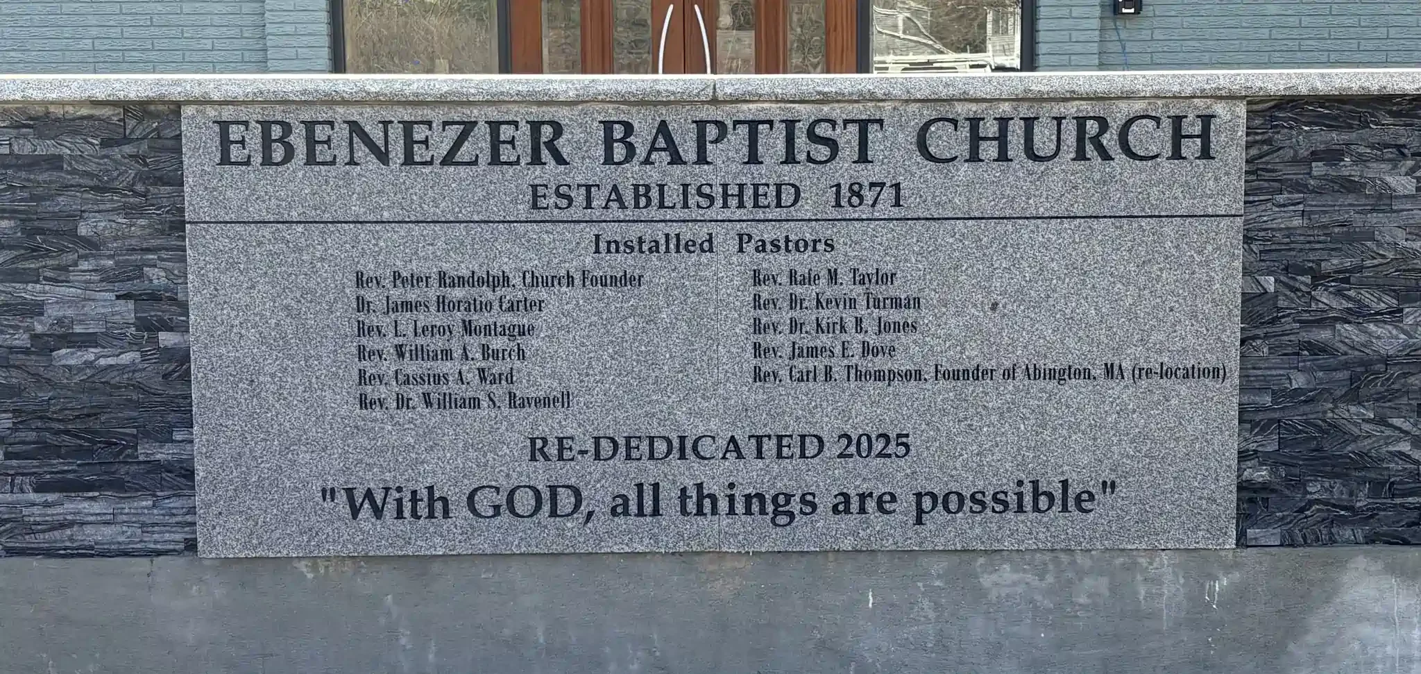 A granite sign in front of a church displaying the name 'Ebenezer Baptist Church', established in 1871, with a list of pastors and a quote from the Bible.