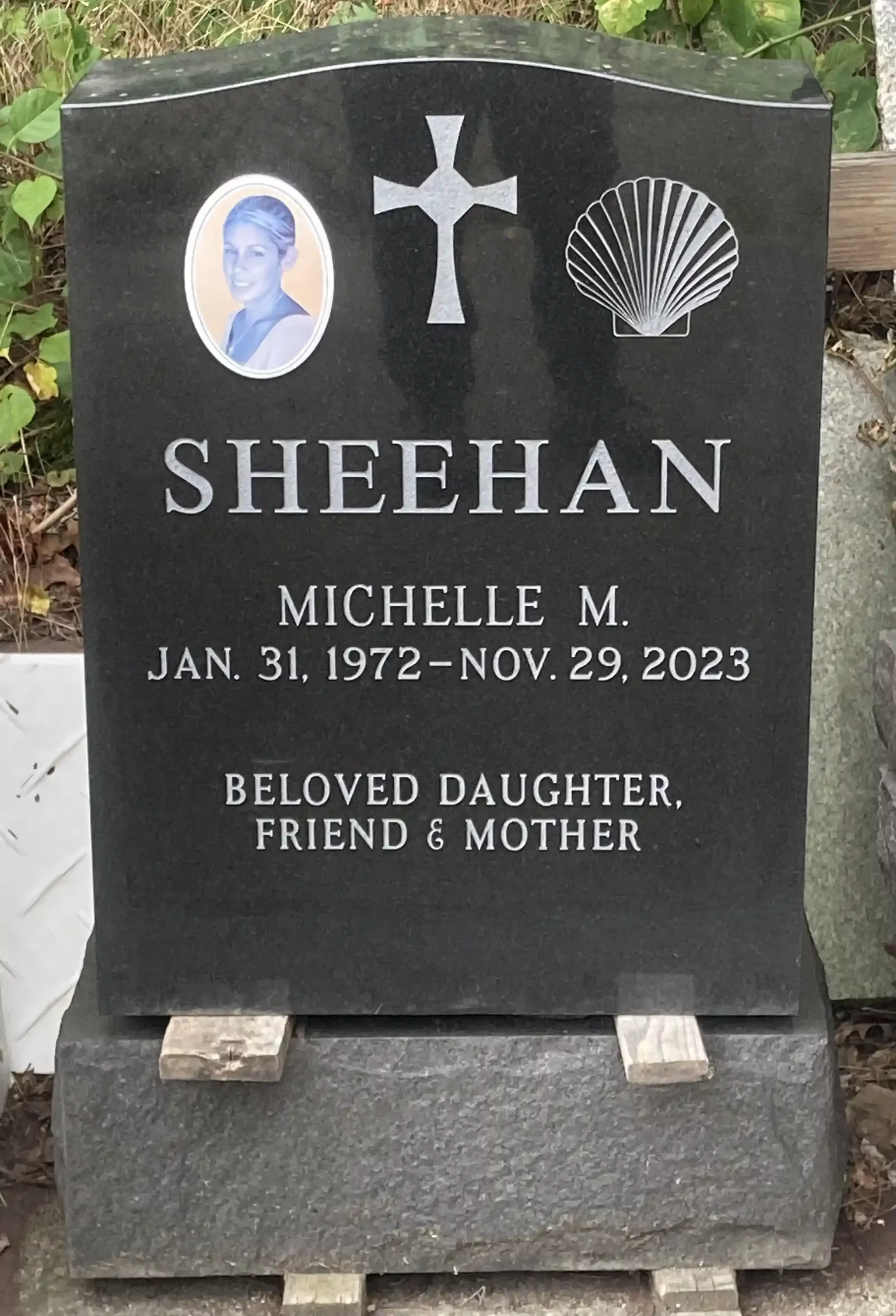Black granite headstone with a portrait, a cross, and a shell symbol. Inscription reading: 'Beloved Daughter, Friend & Mother'.