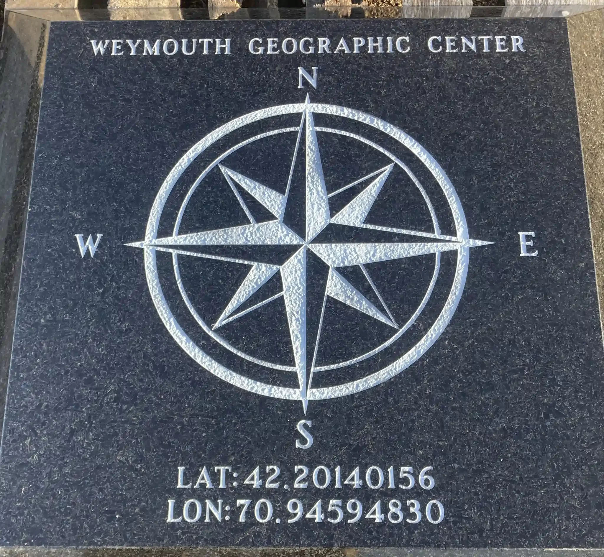 Black granite plaque with white etched compass rose and text reading 'Weymouth Geographic Center'.