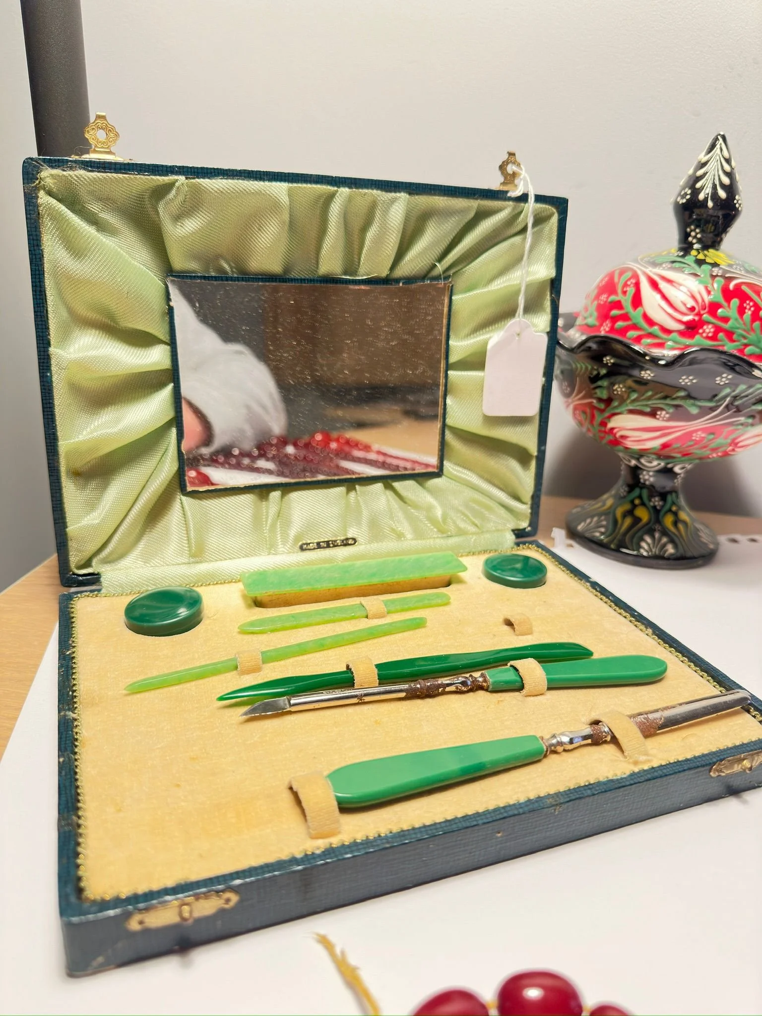 Vintage Green Catalin Nail Set in Case
A vintage case containing a nail care set with tools and jewellery pieces crafted in gorgeous green Catalin, displayed open on a table with a decorative vase in the background. The striking jade-green tones and