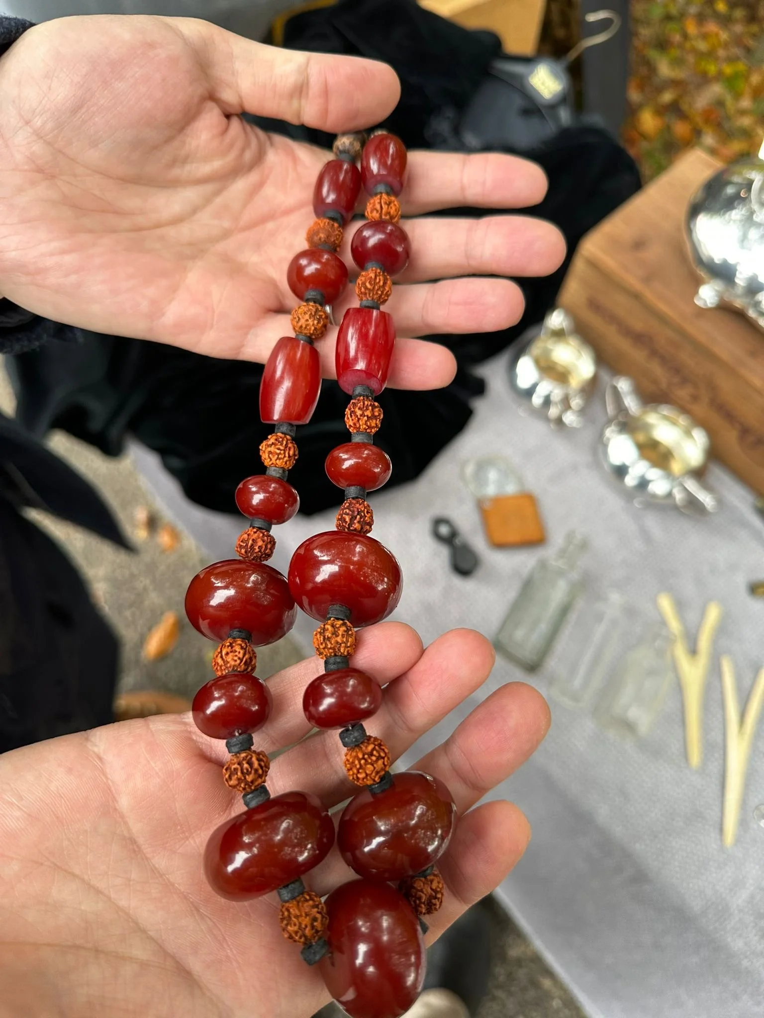 Vintage African Necklace – Bakelite Catalin Beads
A person holding a striking African necklace composed of large red beads and smaller orange beads, crafted from Bakelite Catalin. In the background, other jewellery and silver-coloured objects can be