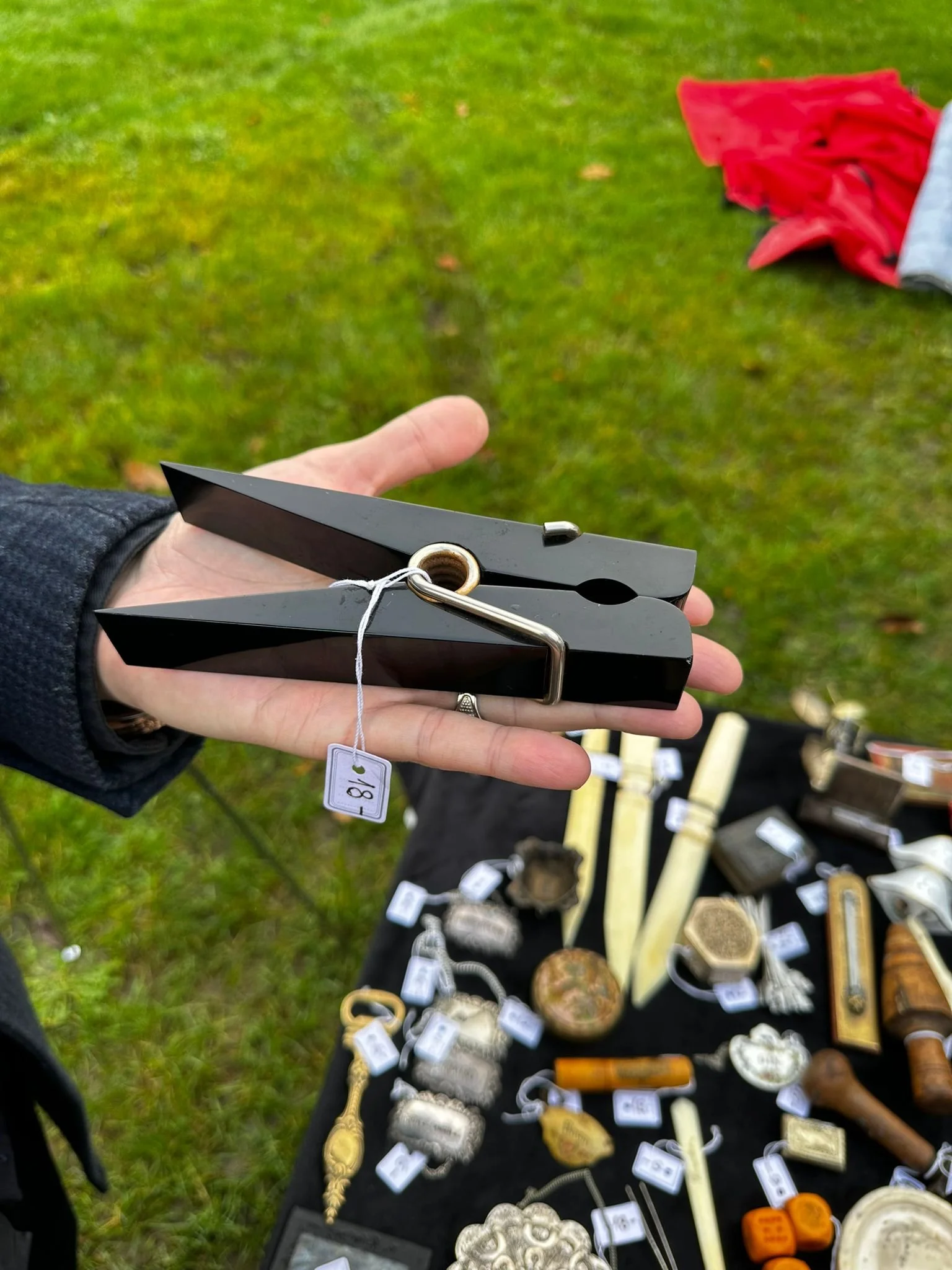 Person holding two black, pointed objects at an outdoor sale with various vintage and antique items laid out on a black cloth table.
