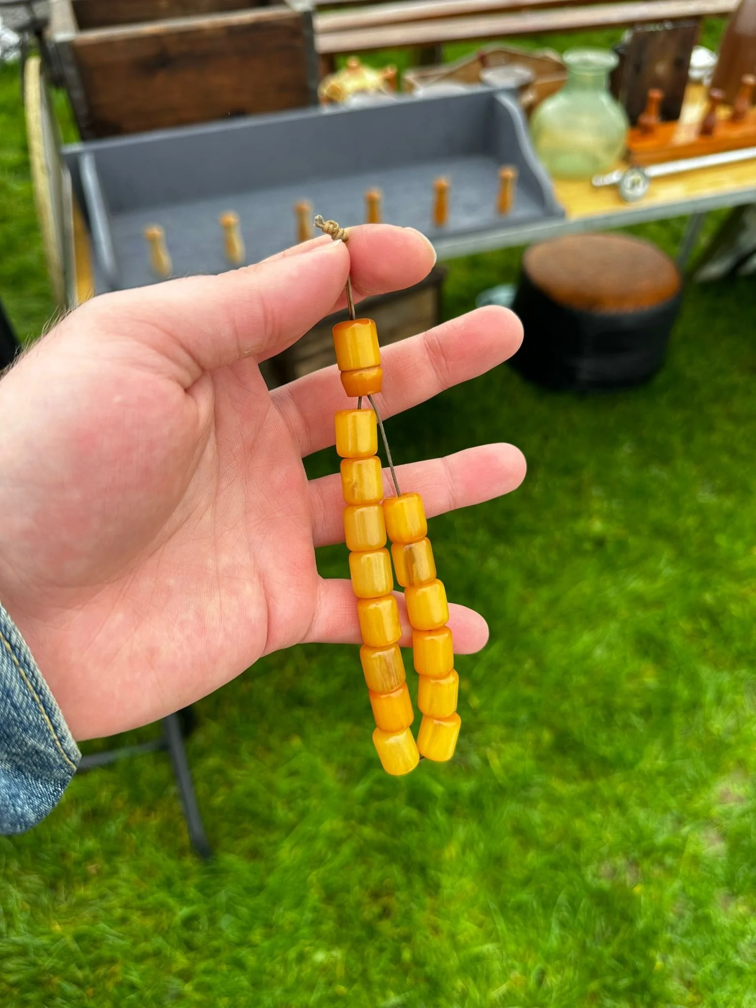 Vintage Catalin (Katalin) Tesbih – Yellow Bead Necklace
A person holding a tesbih (prayer bead necklace) made of striking yellow rectangular Catalin/Katalin beads, shown against an outdoor green grassy background with vintage items displayed on a tab