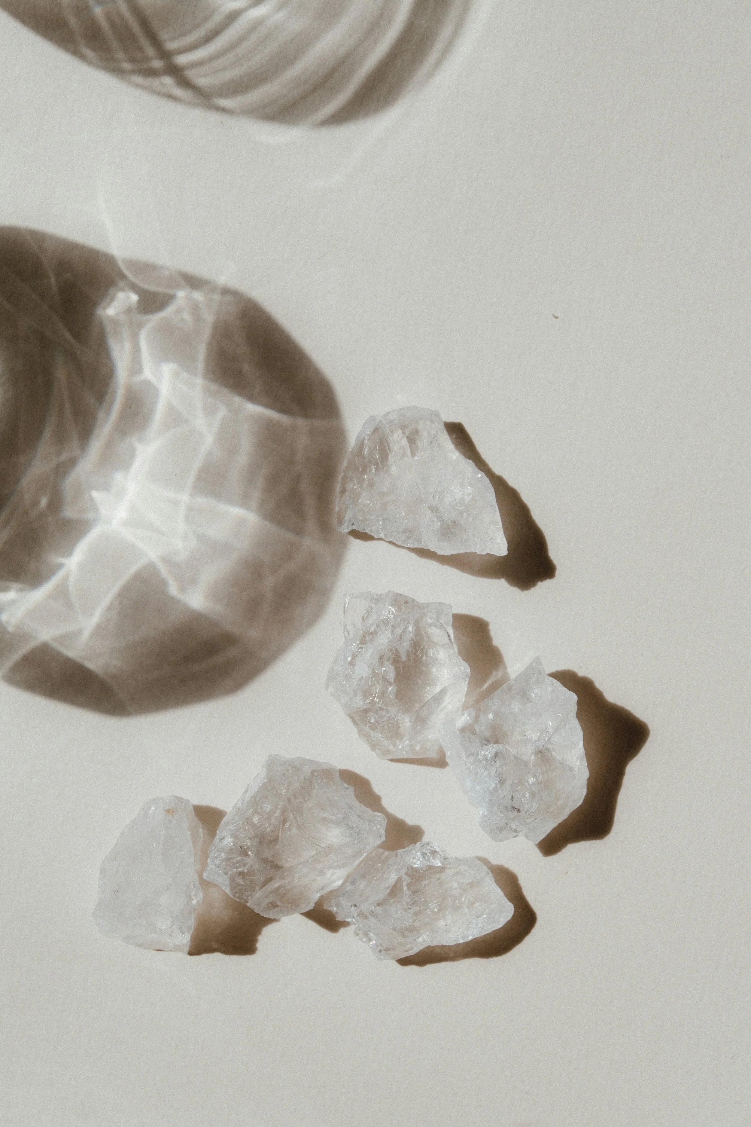 Four large, rough quartz crystals on a light-colored surface with shadows, partially enclosed in a glass container in the upper left corner.