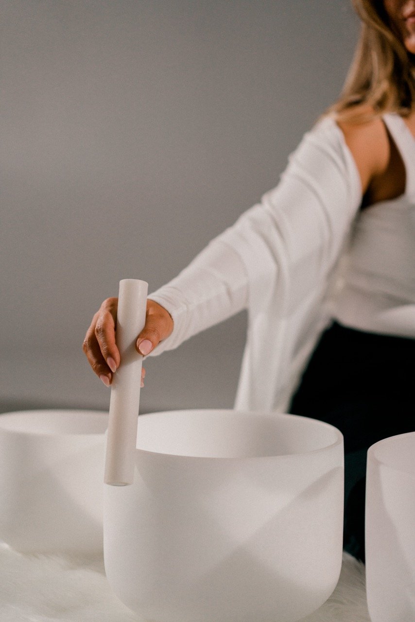 Person wearing a white long-sleeve shirt playing a white singing bowl with a mallet.
