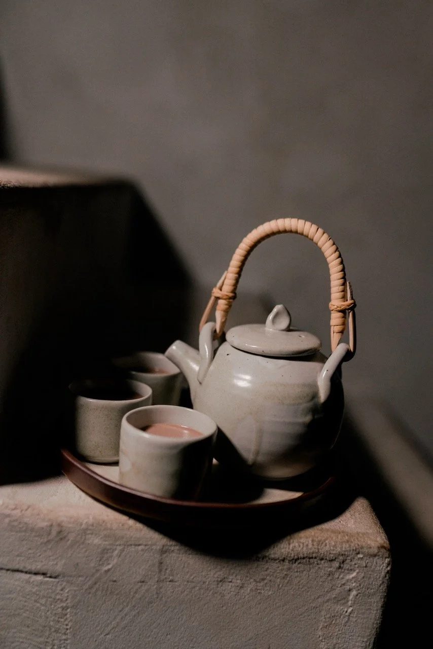 Ceramic teapot and three small cups on a tray, placed on a textured surface with a dark, blurred background.