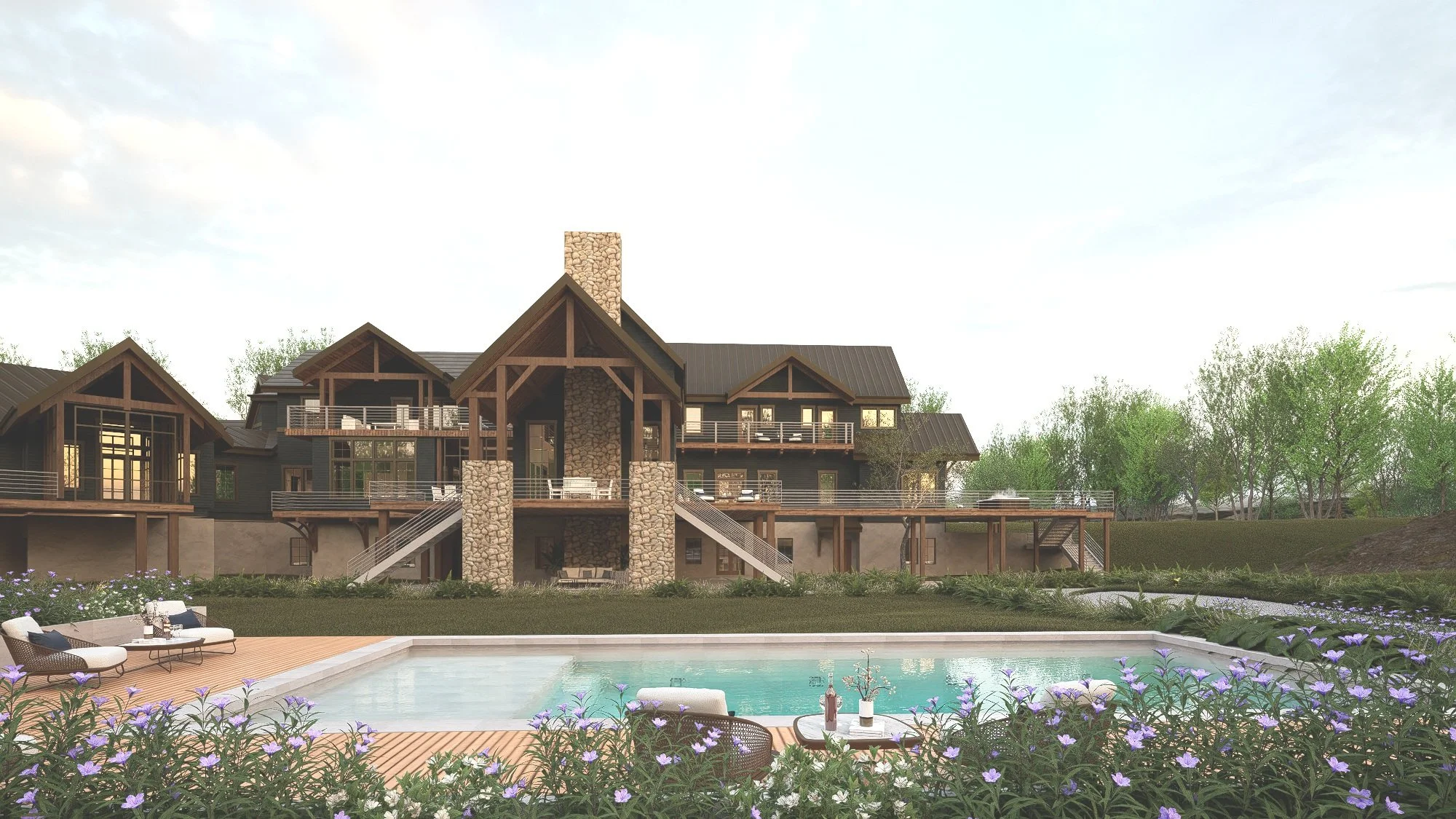A large multi-story house with a stone chimney, multiple decks with railings, and large windows, surrounded by trees. In the foreground, there is a swimming pool with outdoor furniture and purple flowers along the poolside.