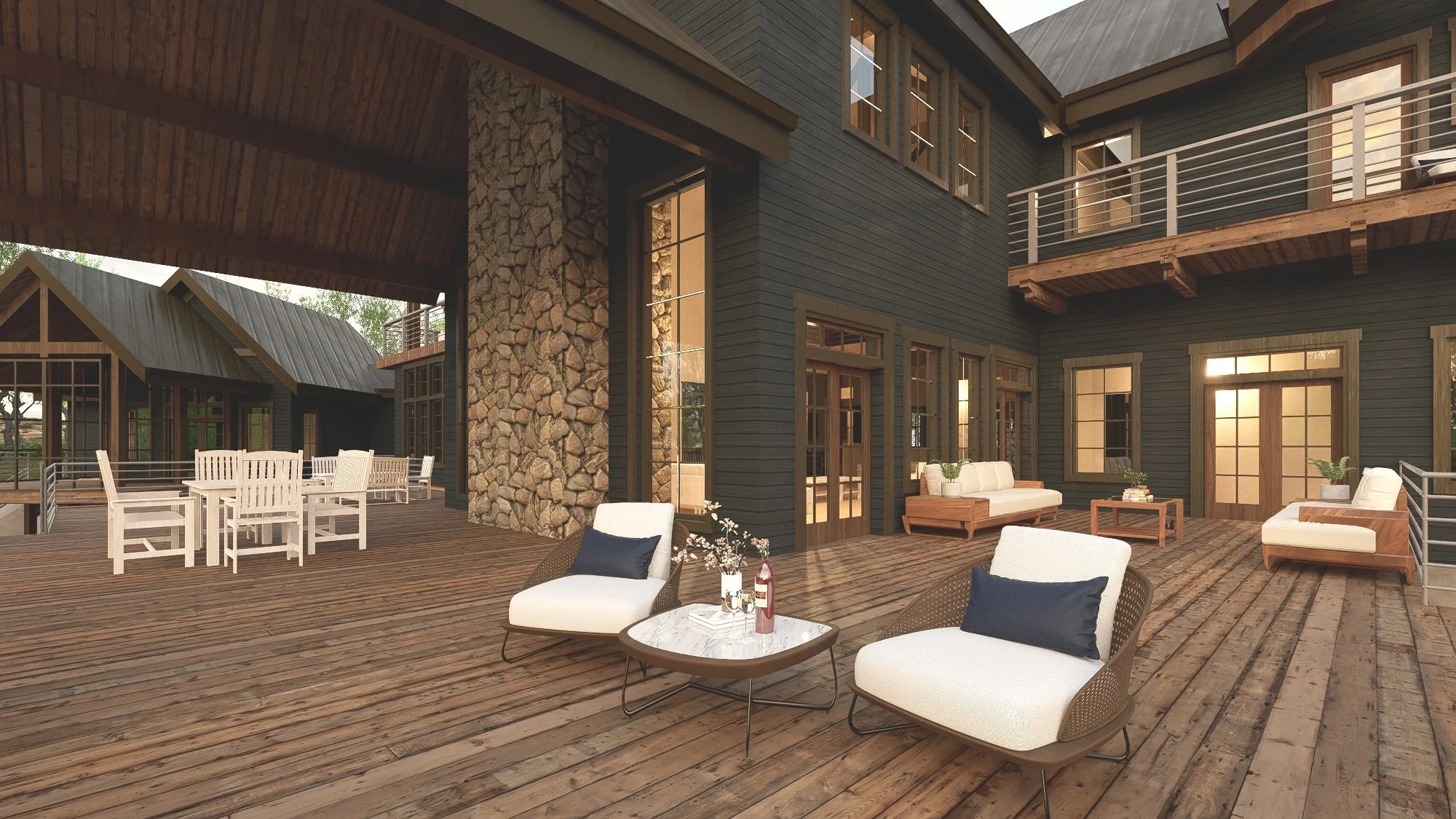 Outdoor wooden patio with seating area, including two white chairs with black pillows, a coffee table with drinks and flowers, and additional chairs and sofas with pillows, against a backdrop of dark wood house walls and a stone chimney.