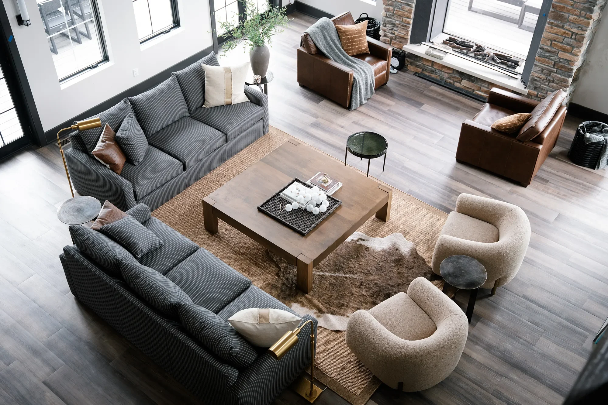 Overview of a modern living room with black and white striped sofa, beige and brown armchairs, a wooden coffee table, and large windows with a brick fireplace.