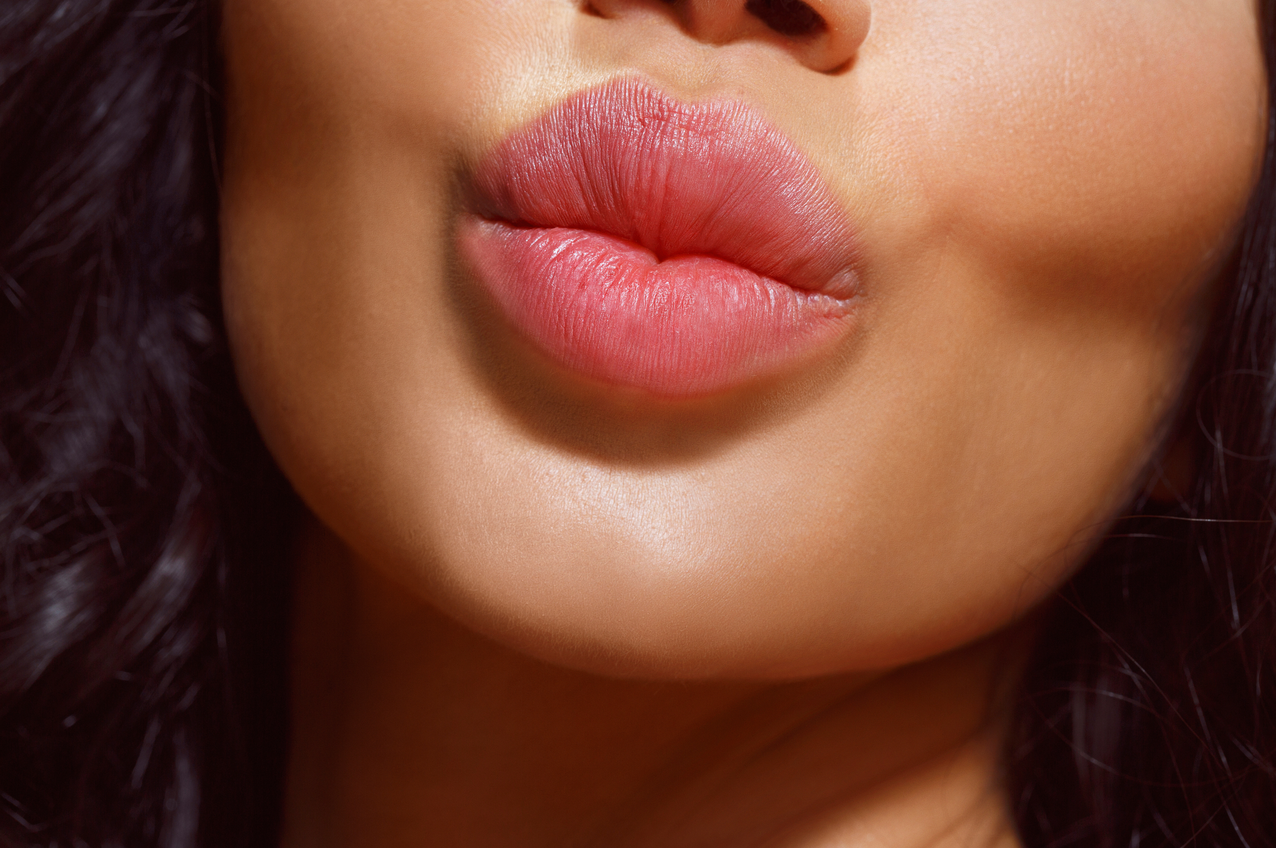 Close-up of a woman's lips with pink lipstick, slightly parted, showing smooth skin and natural texture.