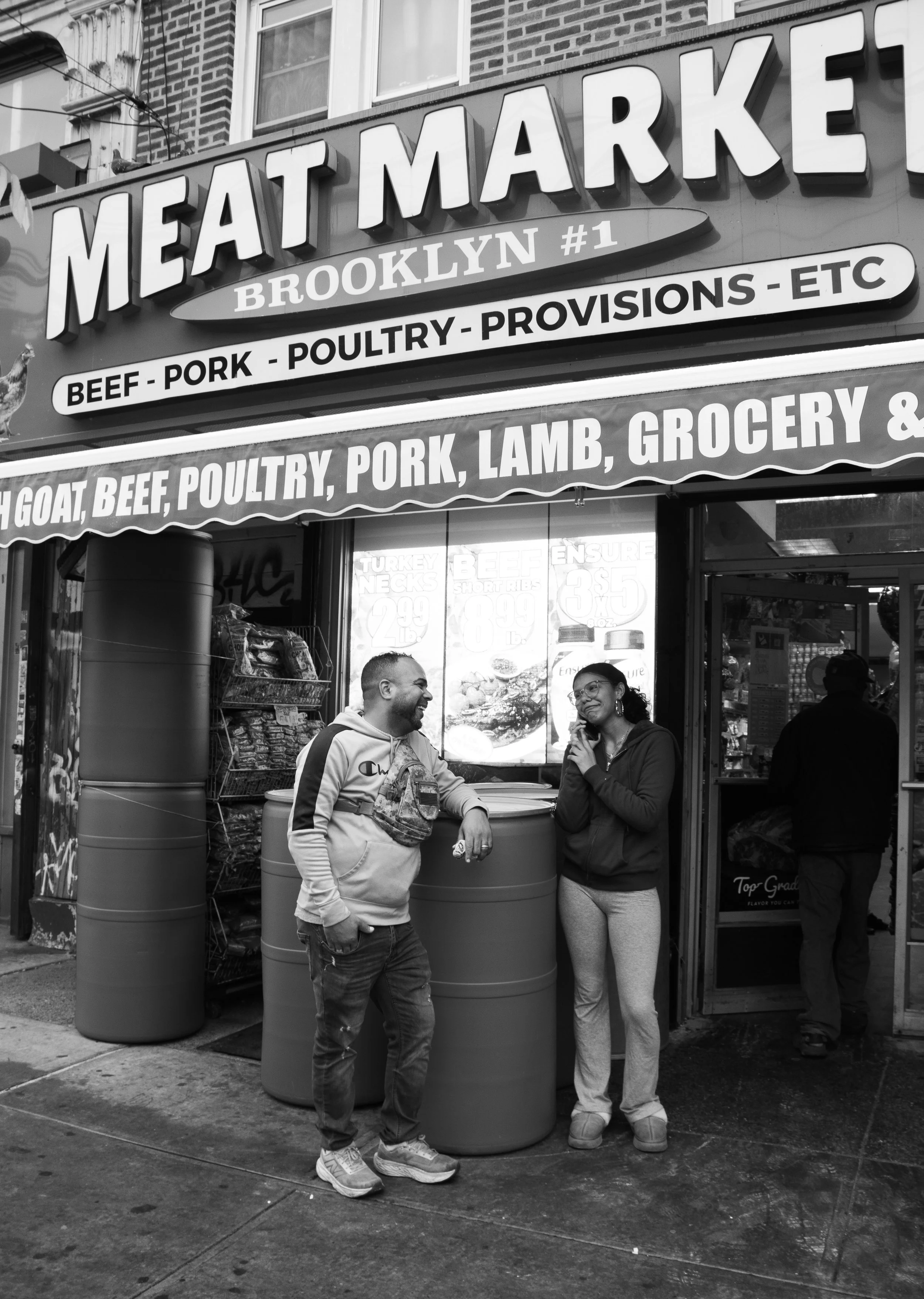 Yinet Arias, "Eldest," 2026. Jairo, in front of his workplace, in East Flatbush, Brooklyn, New York. Having a laugh at his eldest daughter.