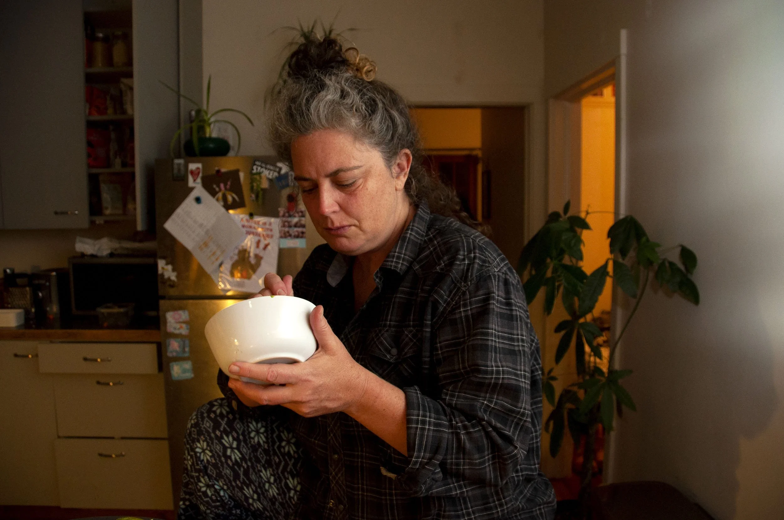 Finn Brooks , "The Final Bite," 2023. After a long day of work, cooking, and stress my mom enjoys her final bite of food in the empty kitchen. My parents' separation has had an enormous toll on my mom. She now juggles all the food preparation, cleani