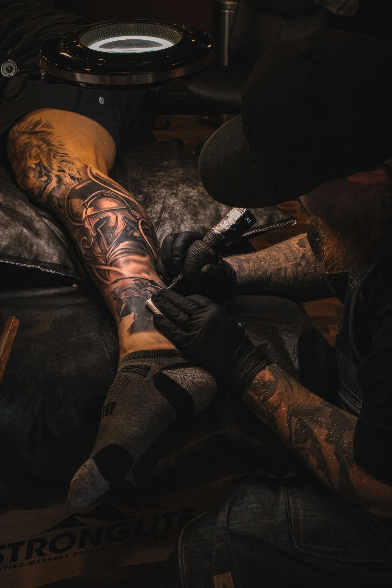 Aiden Yarnal, "The Spartan," 2024. This picture shows my dad tattooing one of his longtime clients' calves, showcasing what he does to provide for my family and pay the bills.