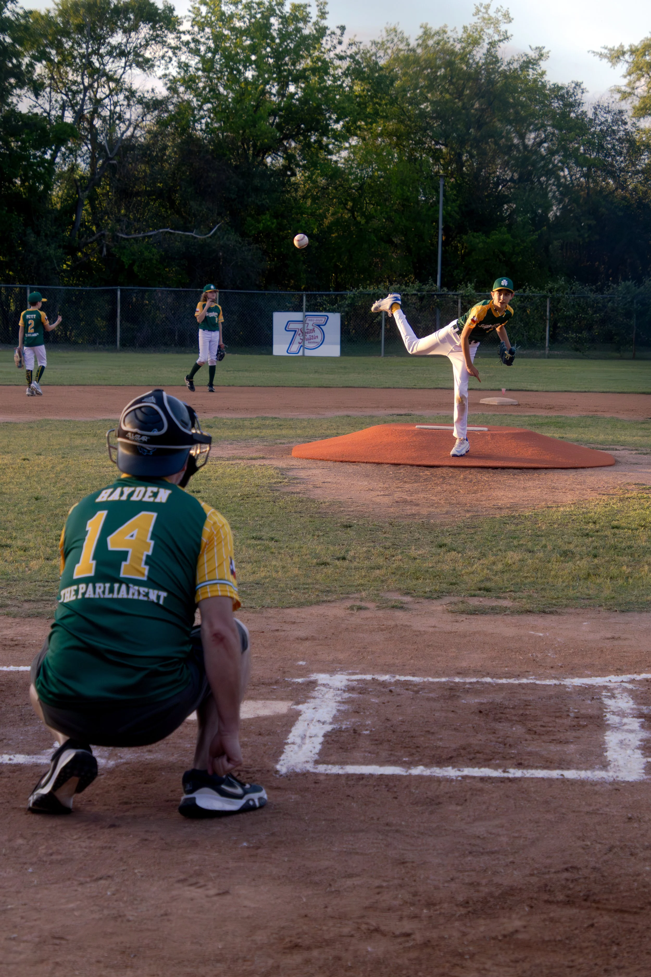 Kiran Hayden, "Fastball," 2026. As my brother hurls a 40-mile-per-hour fastball from the pitcher’s mound across the diamond, my dad stands ready on home plate to catch it, serving as my brother’s warm-up catcher so he can pitch at his baseball game. 