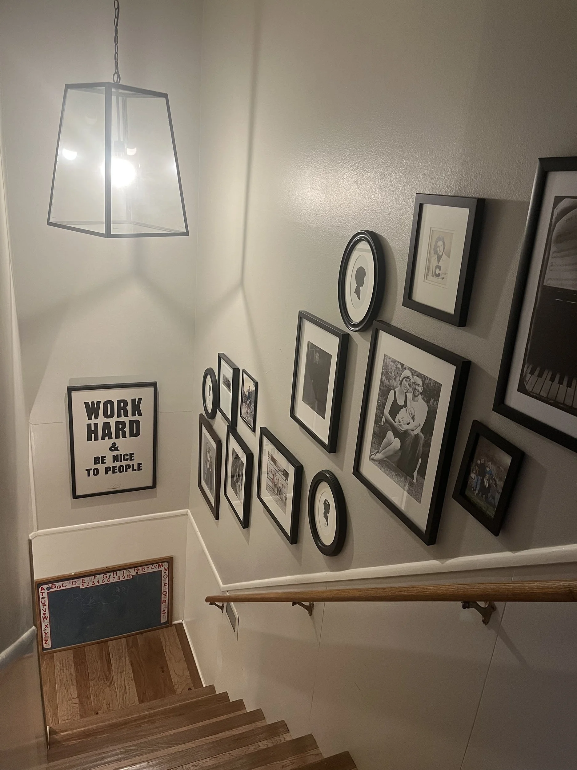 Stella Little, "Stairway," 2023. 
A wall of important family pictures from multiple decades ago to the present day. They lead to a motivational sign that keeps everyone thinking about the predominant message of working hard while still being nice to