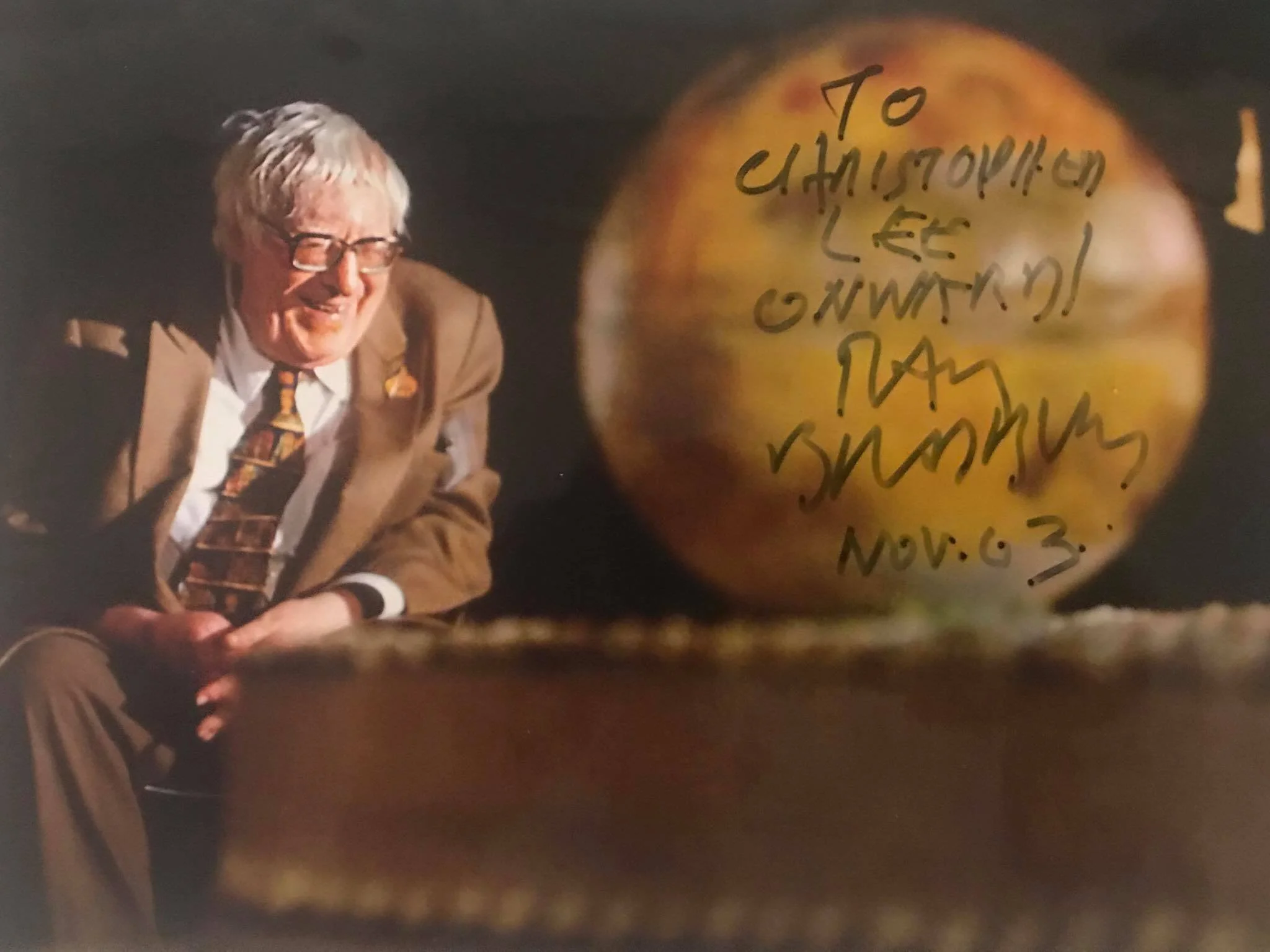 Photo of author Ray Bradbury smiling in a suit beside a signed inscription to Christopher Lee with the word “Onward,” a story featured in the book The Story Comes First.