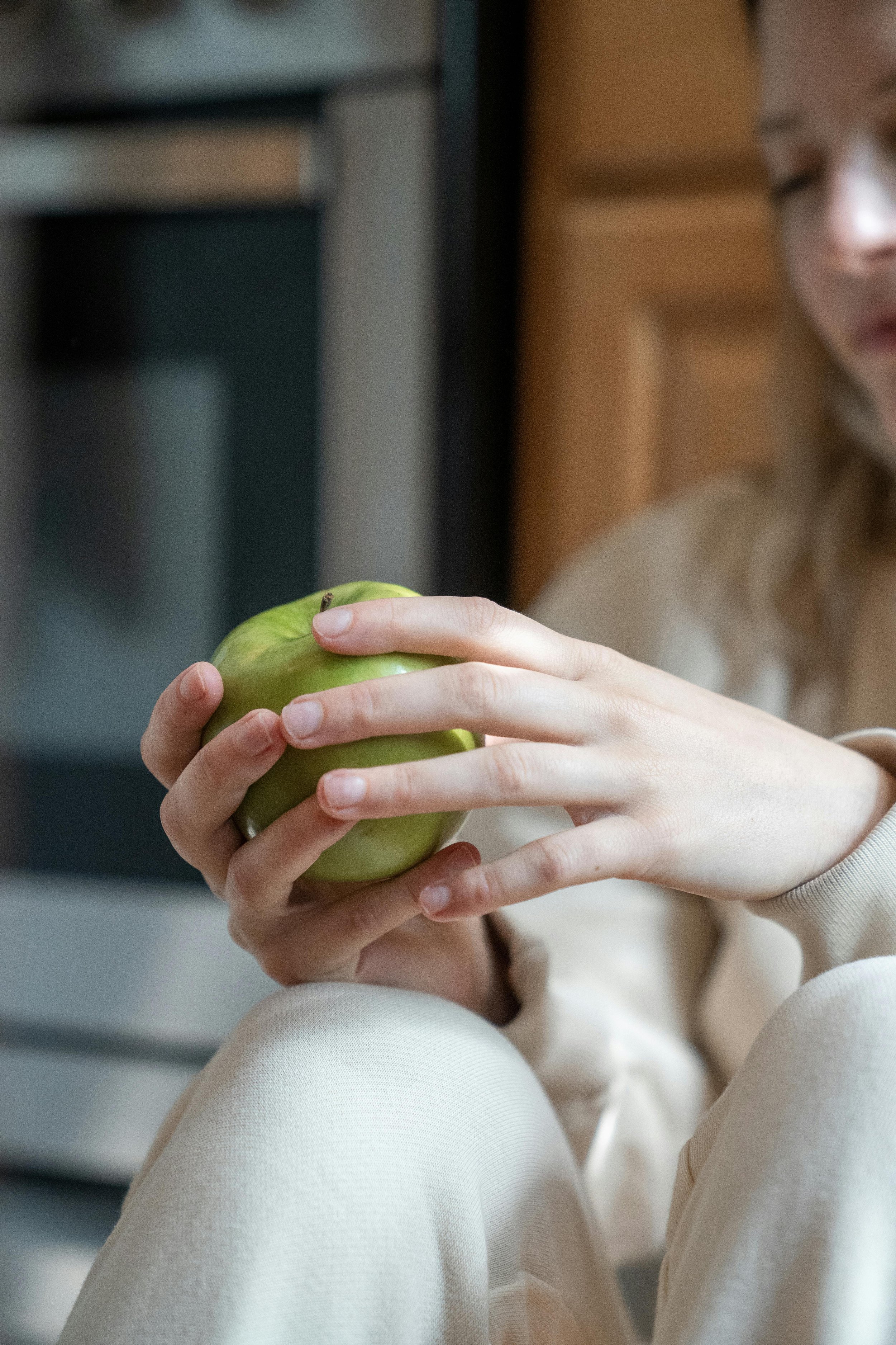 A person holding a green apple with both hands while sitting down, with part of their face slightly visible on the right side of the image.
