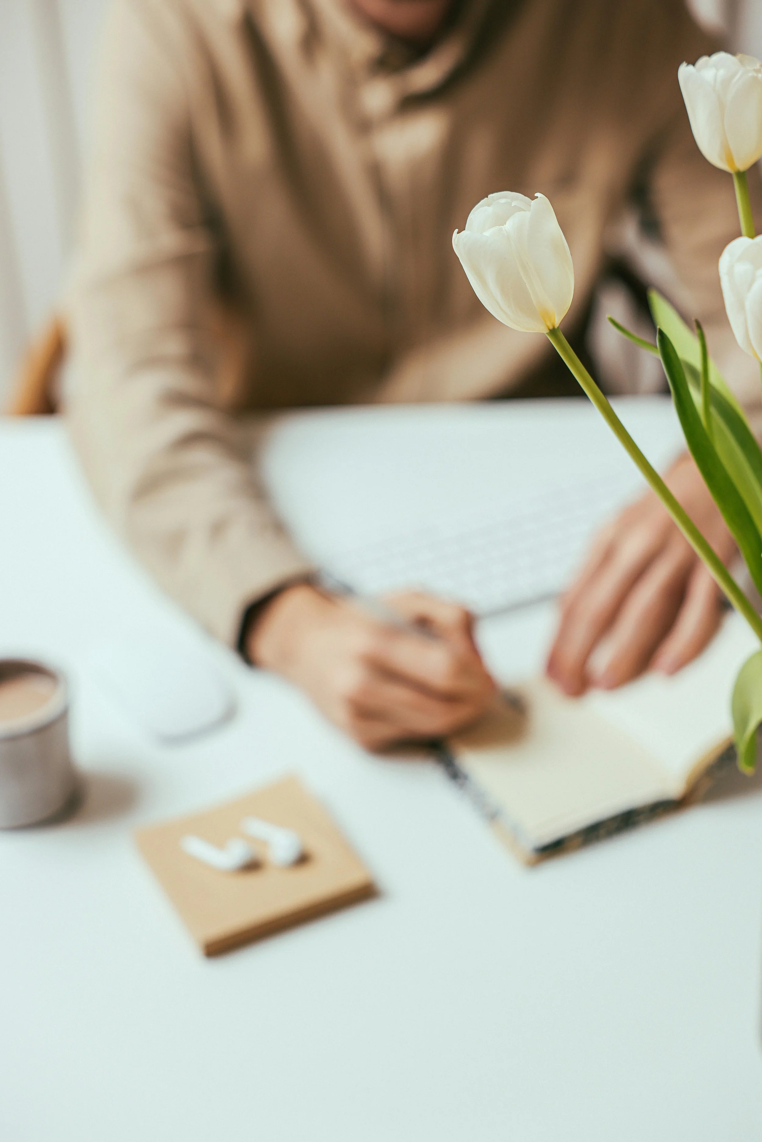Close-up of white tulips on a table in front of a person writing in a notebook.