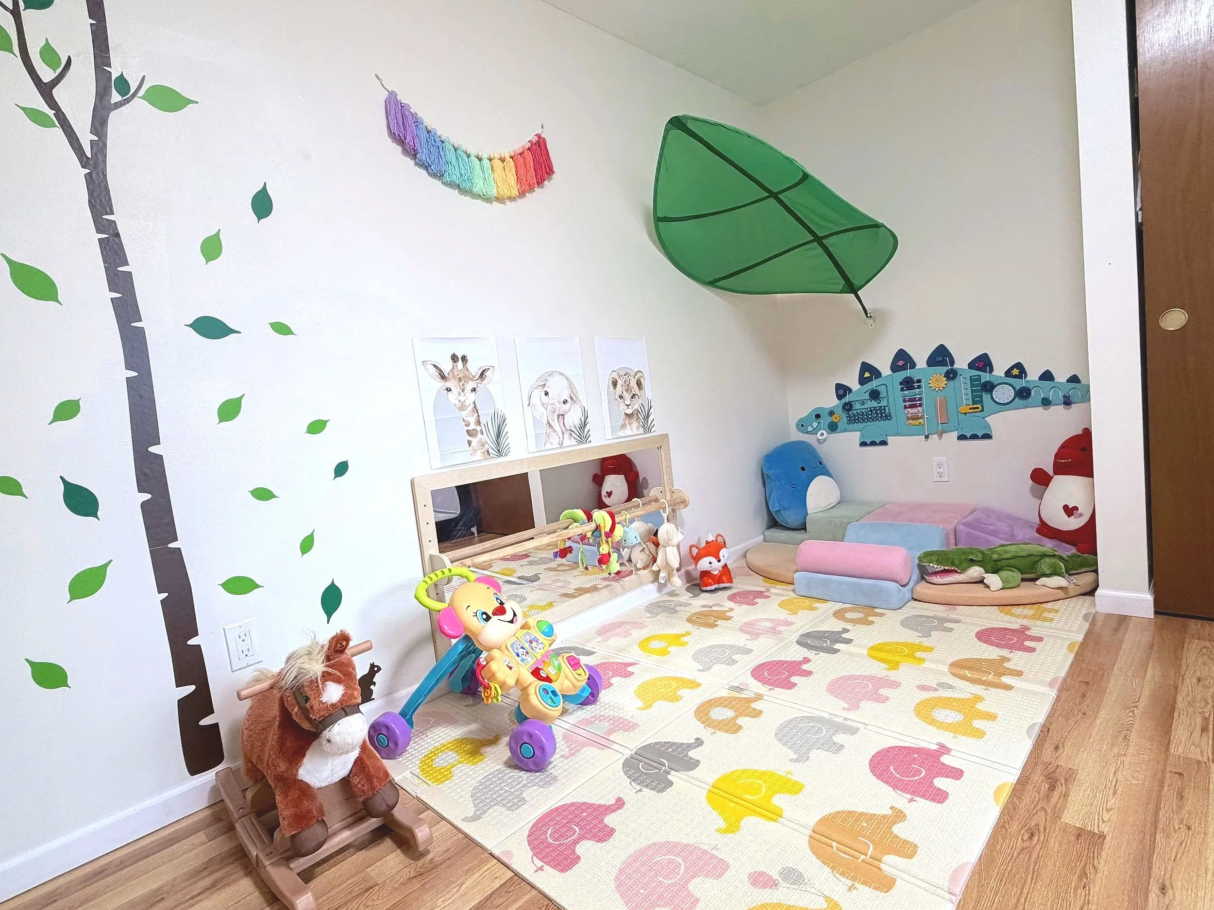 Colorful children's playroom with animal-themed carpet, toys, stuffed animals, wall decals, and a small bed with plush cushions.