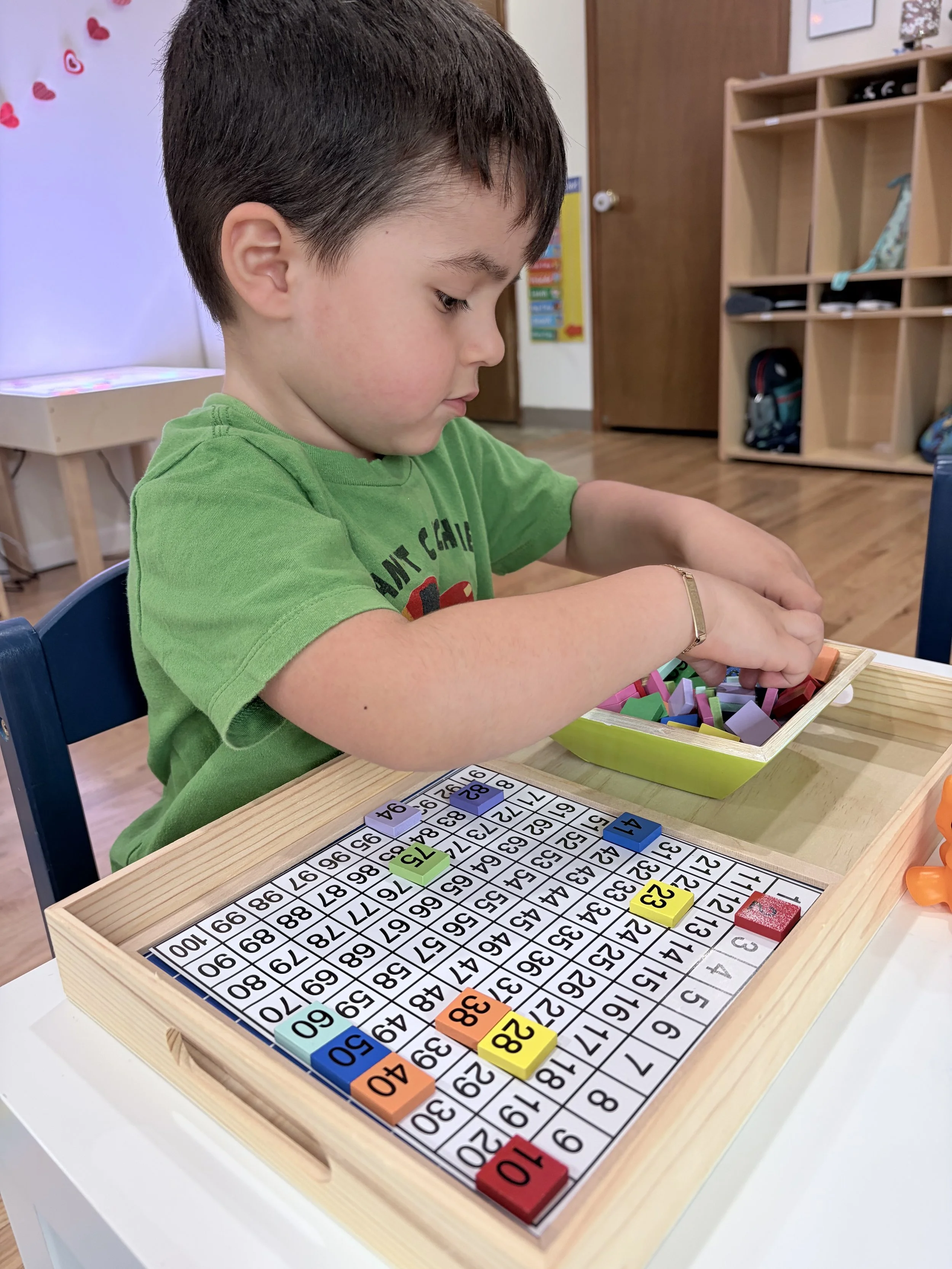 A young boy playing with a number board game at a table in a classroom.