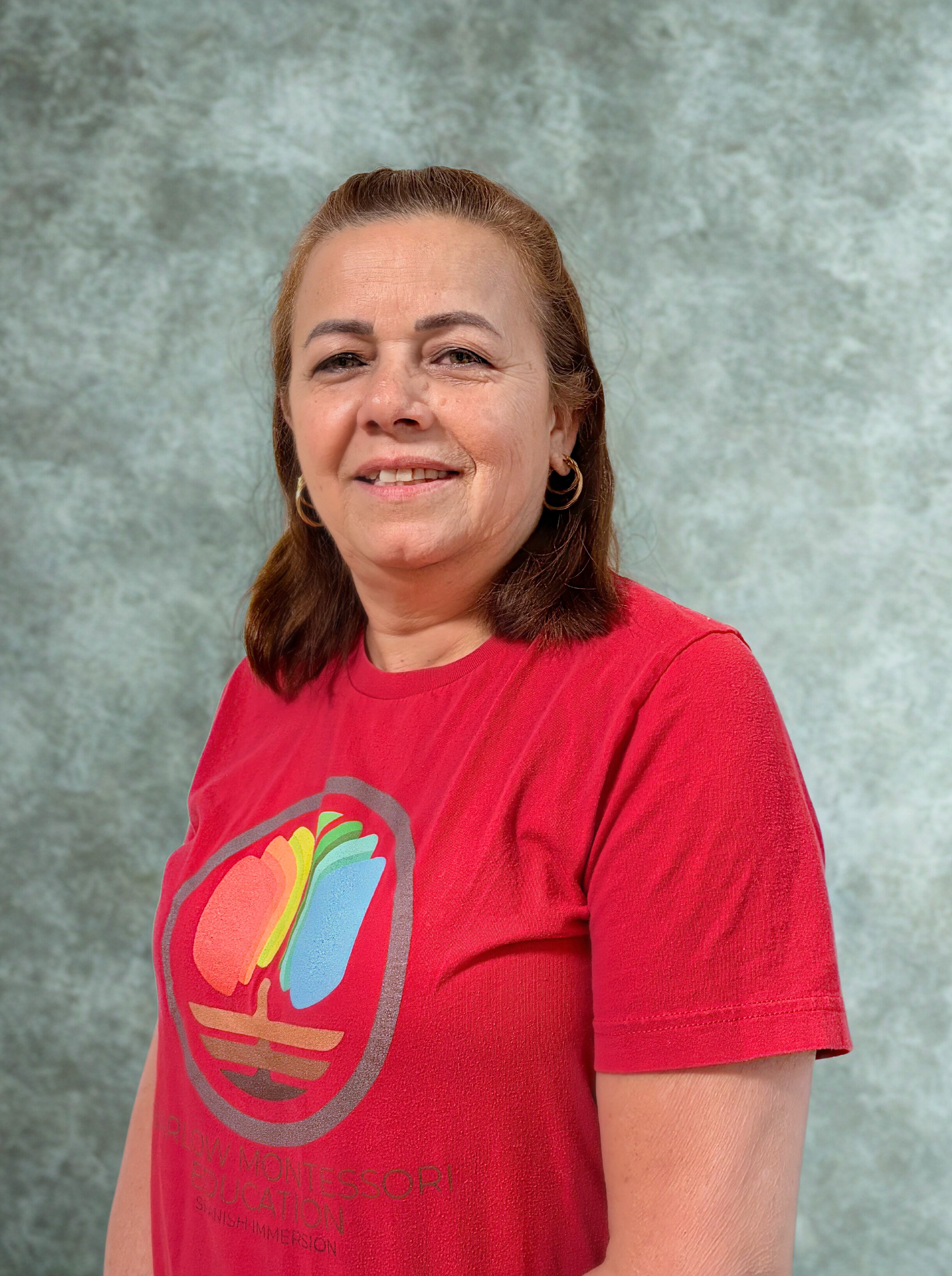 Smiling woman with dark hair wearing a white blazer and blue top against a plain background.