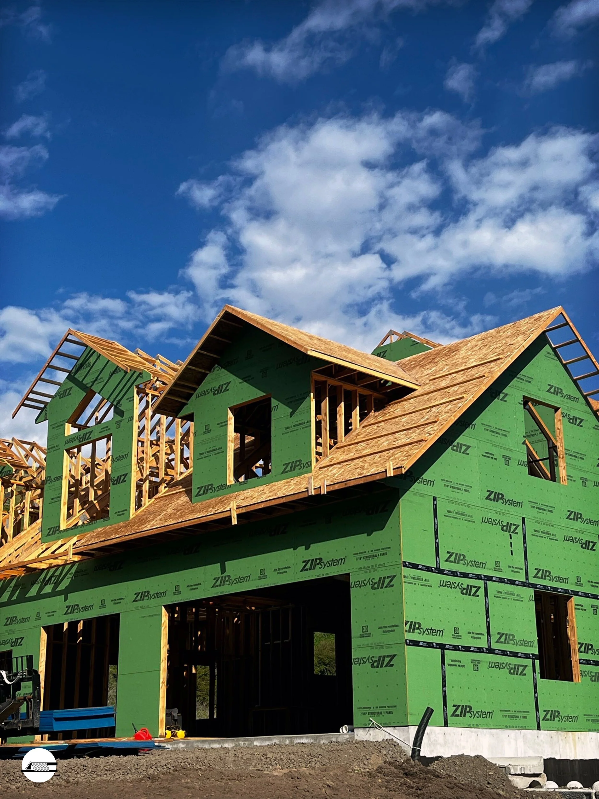 Under construction house with green sheathing and wooden roof framework, partly completed with visible framing and open windows.
