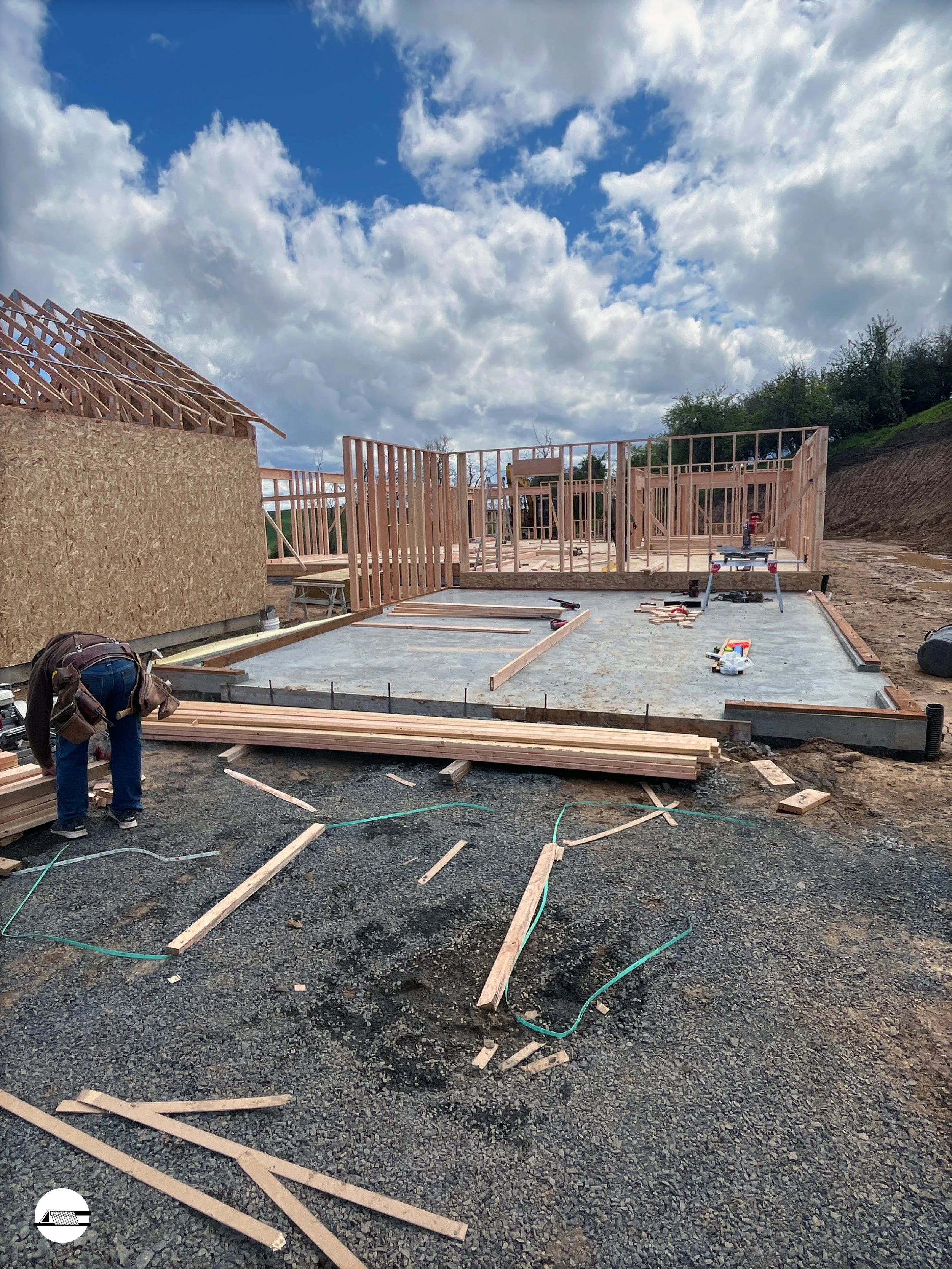 Construction site with wooden framing for a house under a partly cloudy sky.