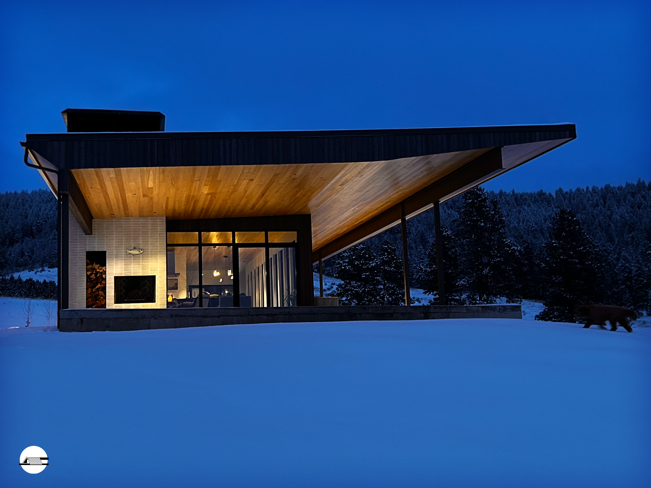 Modern house with large glass windows and wooden ceiling in a snowy landscape at night