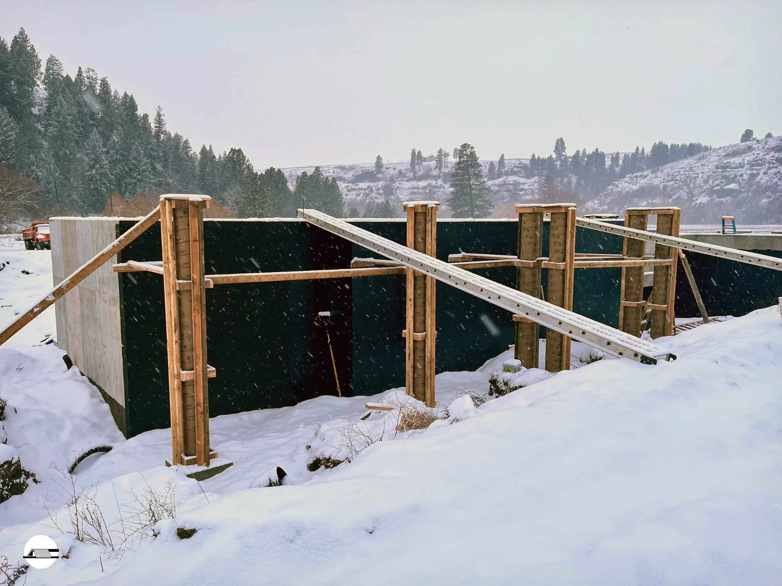 Construction site in a snowy landscape showing wooden framing and black sheathing for a building under construction.