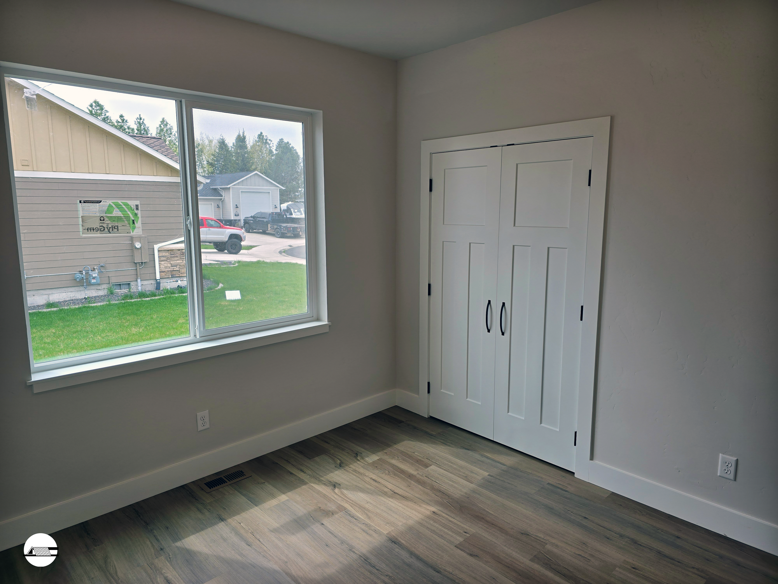 Empty room with a large window, white closet doors, light wood flooring, and a beige wall in a house under construction.