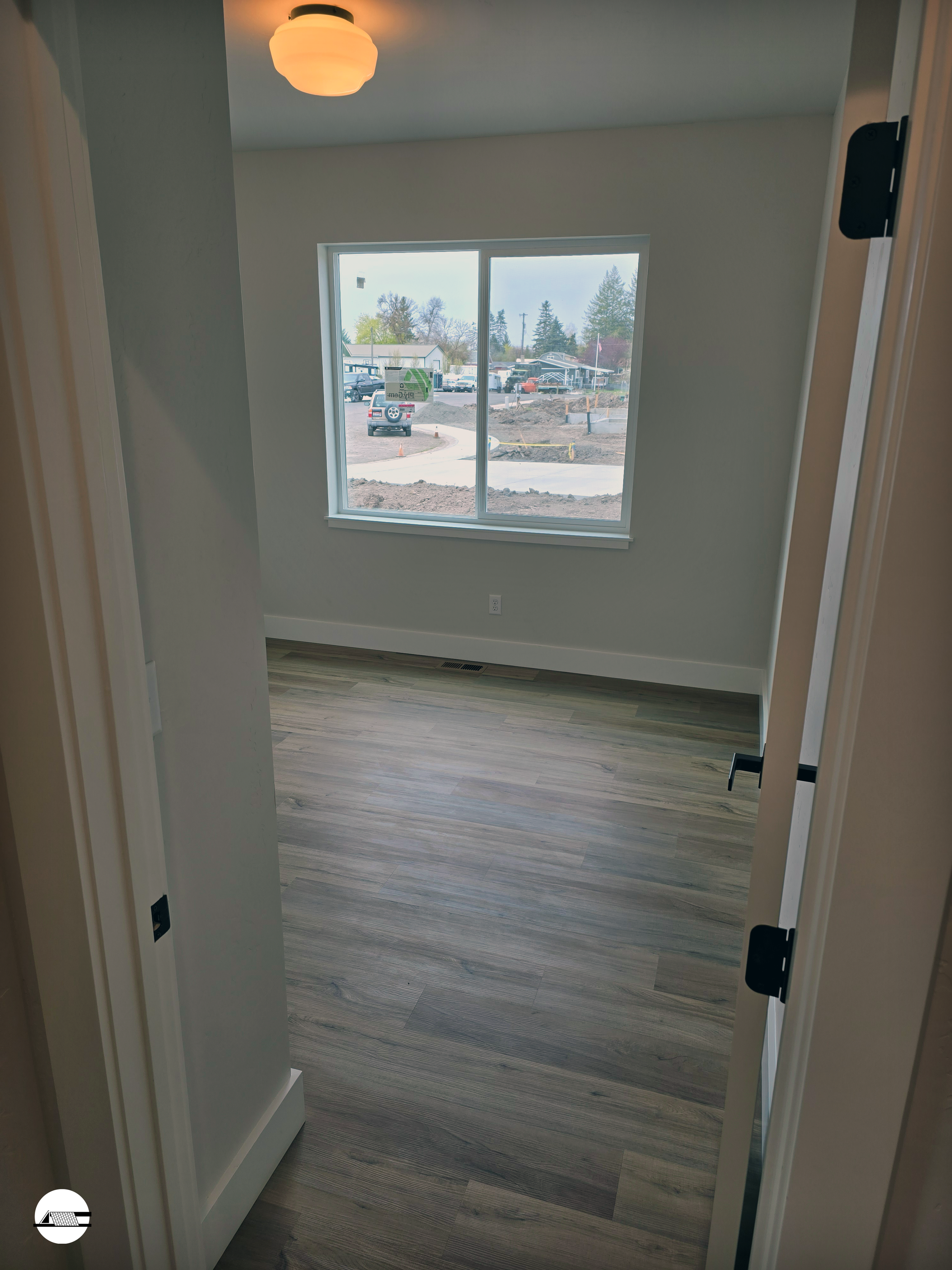 Empty room with wood flooring, a window, and a ceiling light fixture, overlooking an outdoor construction site.
