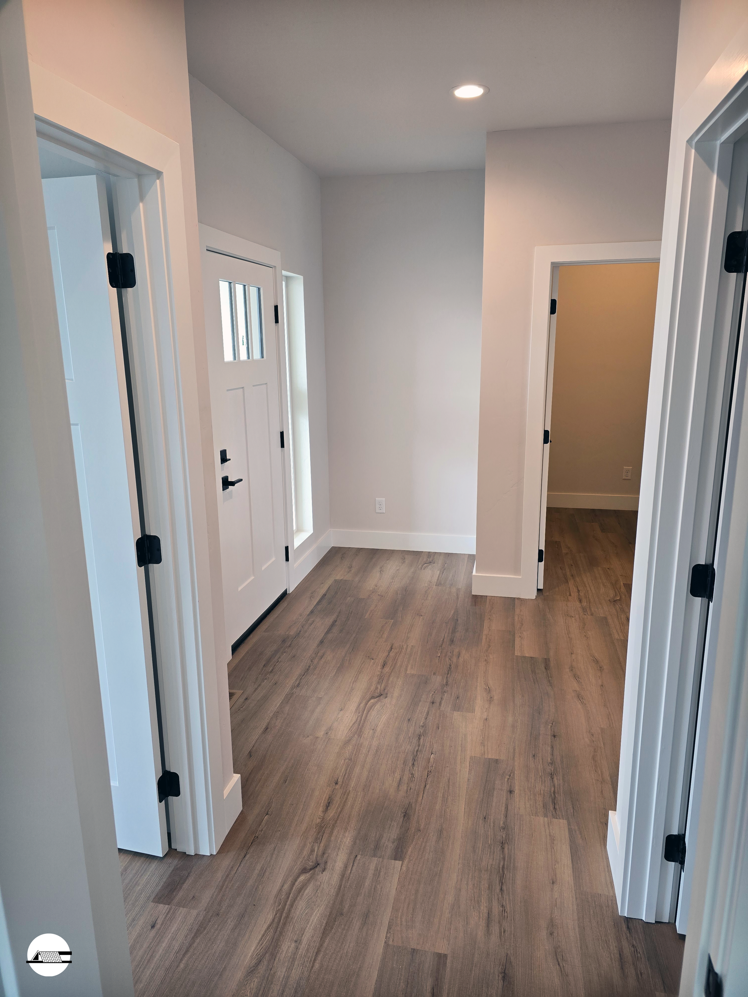 Empty hallway in a modern home with light walls, white door frames, and wood flooring.