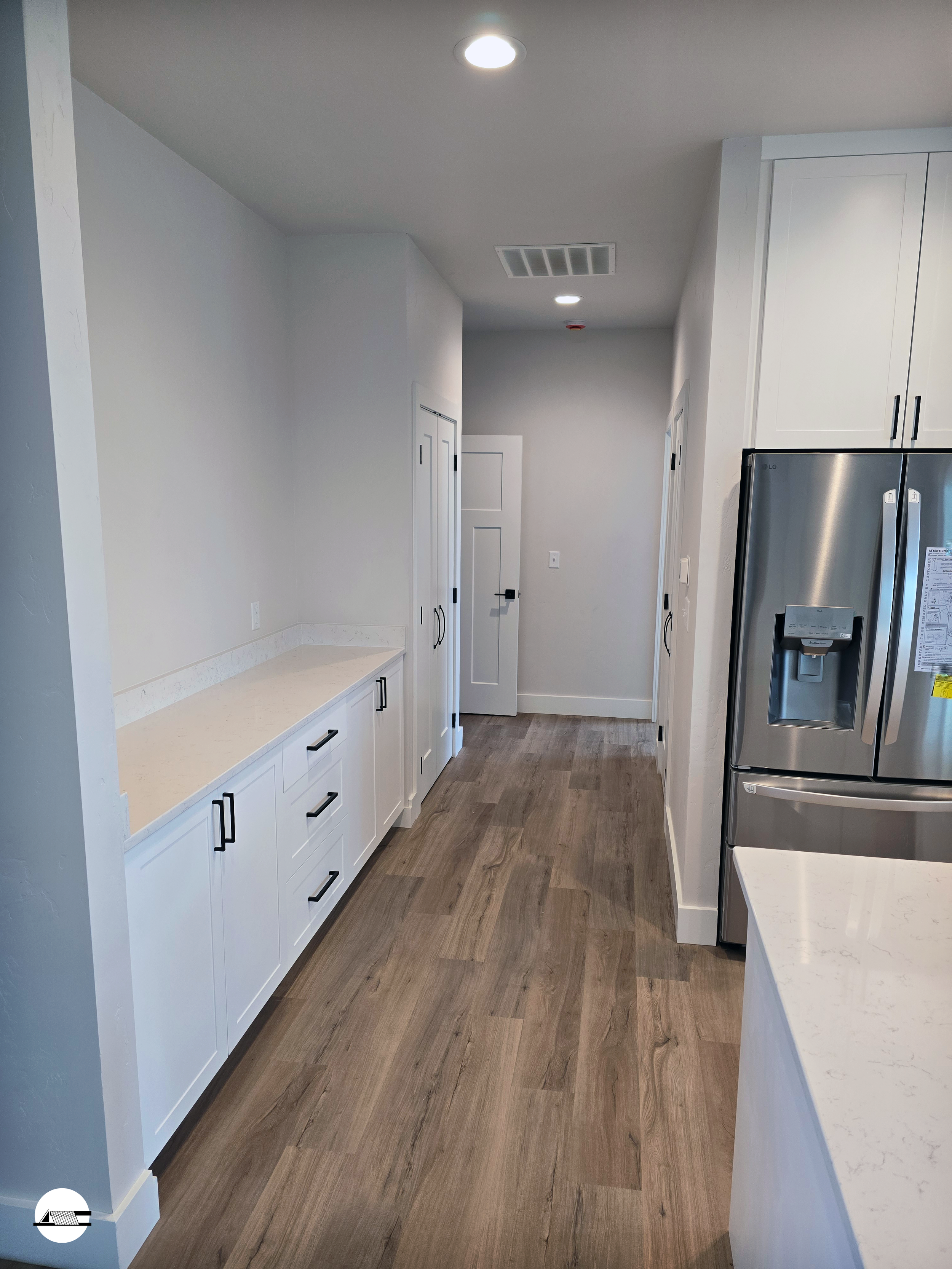 Modern kitchen with white cabinets, stainless steel refrigerator, light wood floors, and recessed ceiling lights.