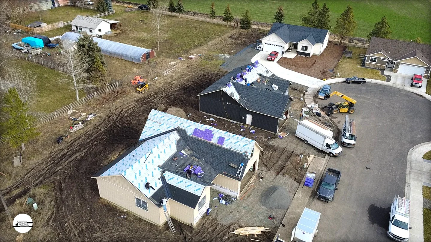 Newly constructed spec house with white siding, black roof and attached garage looking up the driveway.