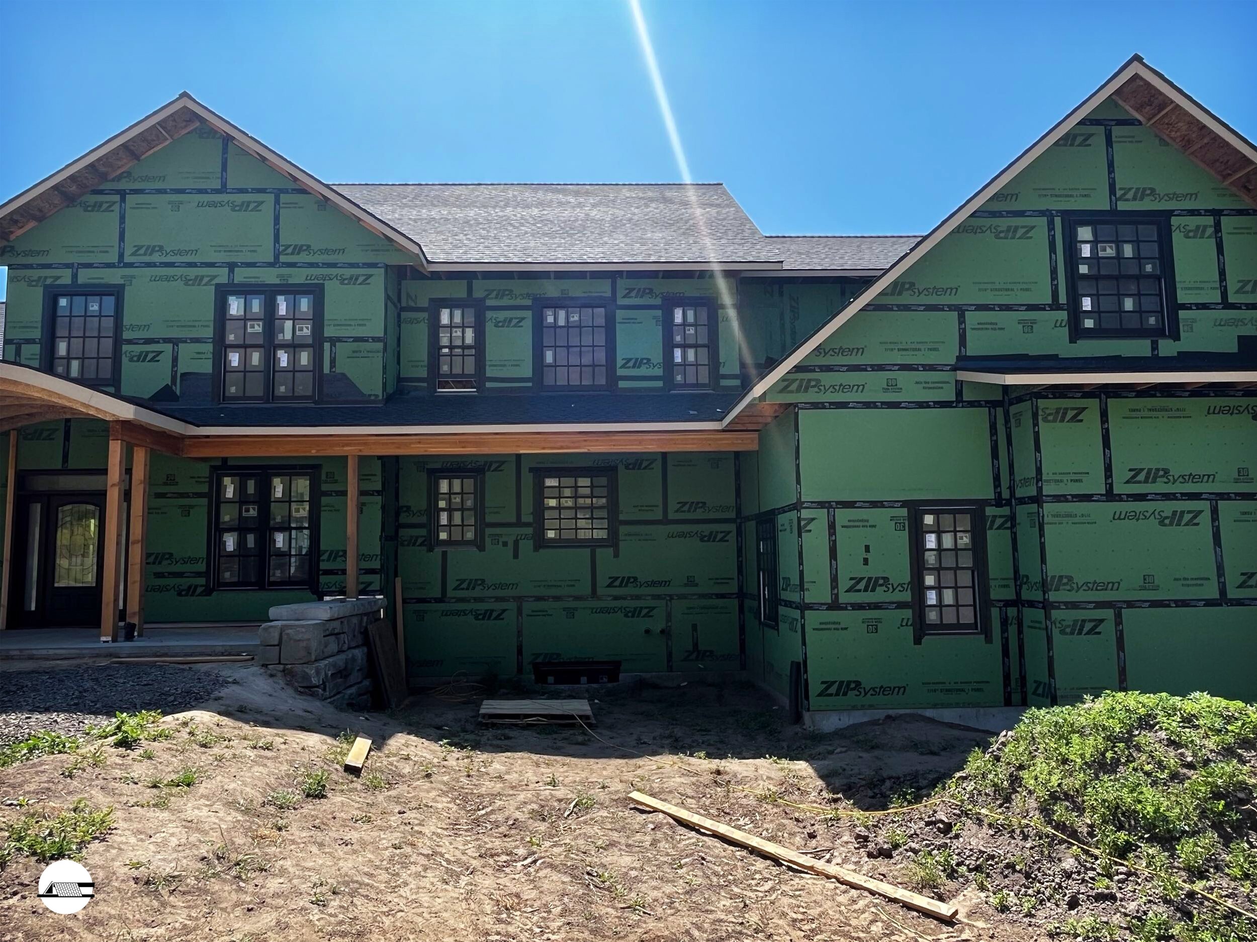 Under-construction house with green sheathing, black-framed windows, and a partially finished patio, under a clear blue sky.