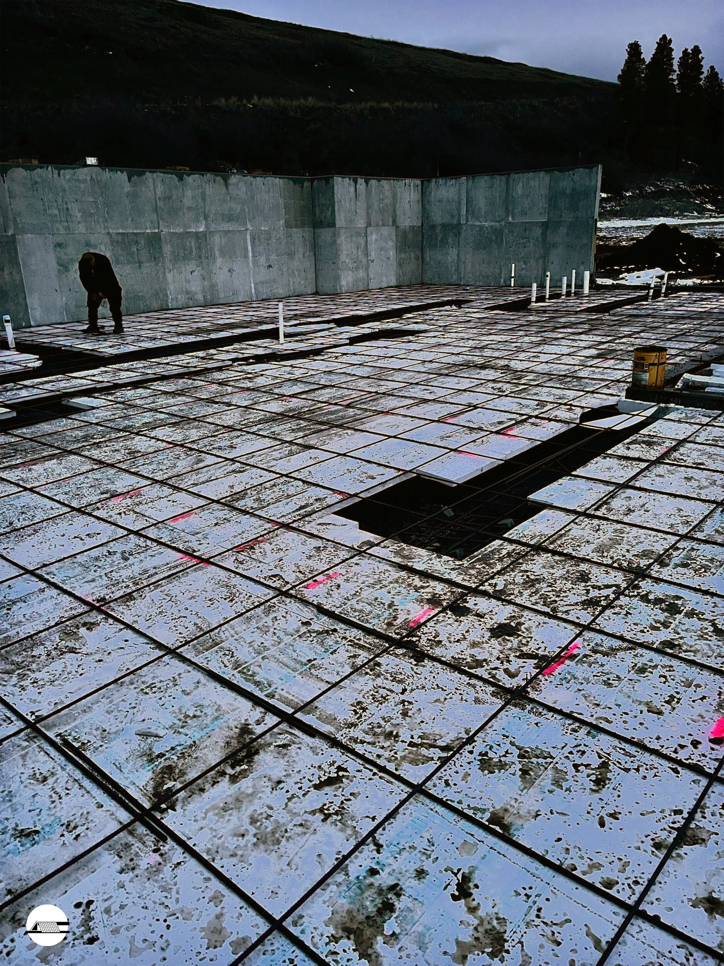 Construction worker on a building site installing steel rebar on a concrete slab with a cityscape in the background.